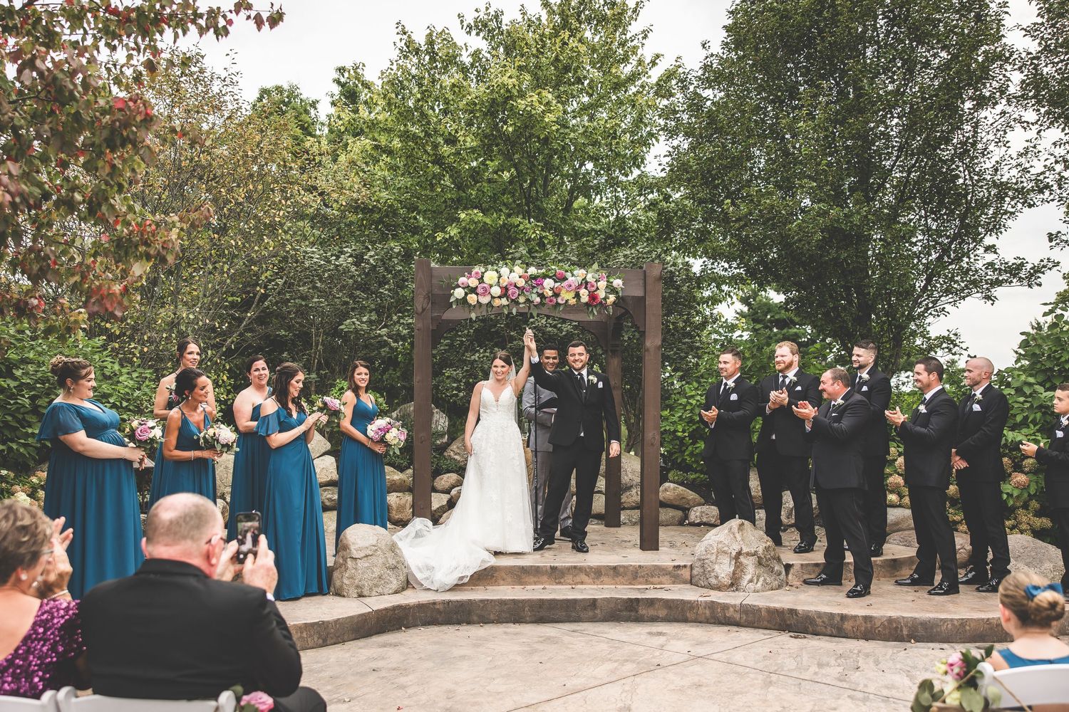 Panoramic view of outdoor wedding ceremony with guests seated on white chairs.