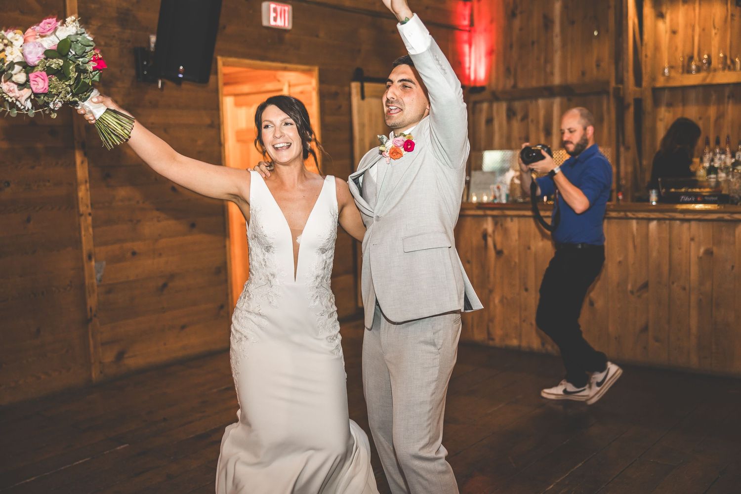 Wedding couple celebrating during reception inside rustic barn venue with string lights.