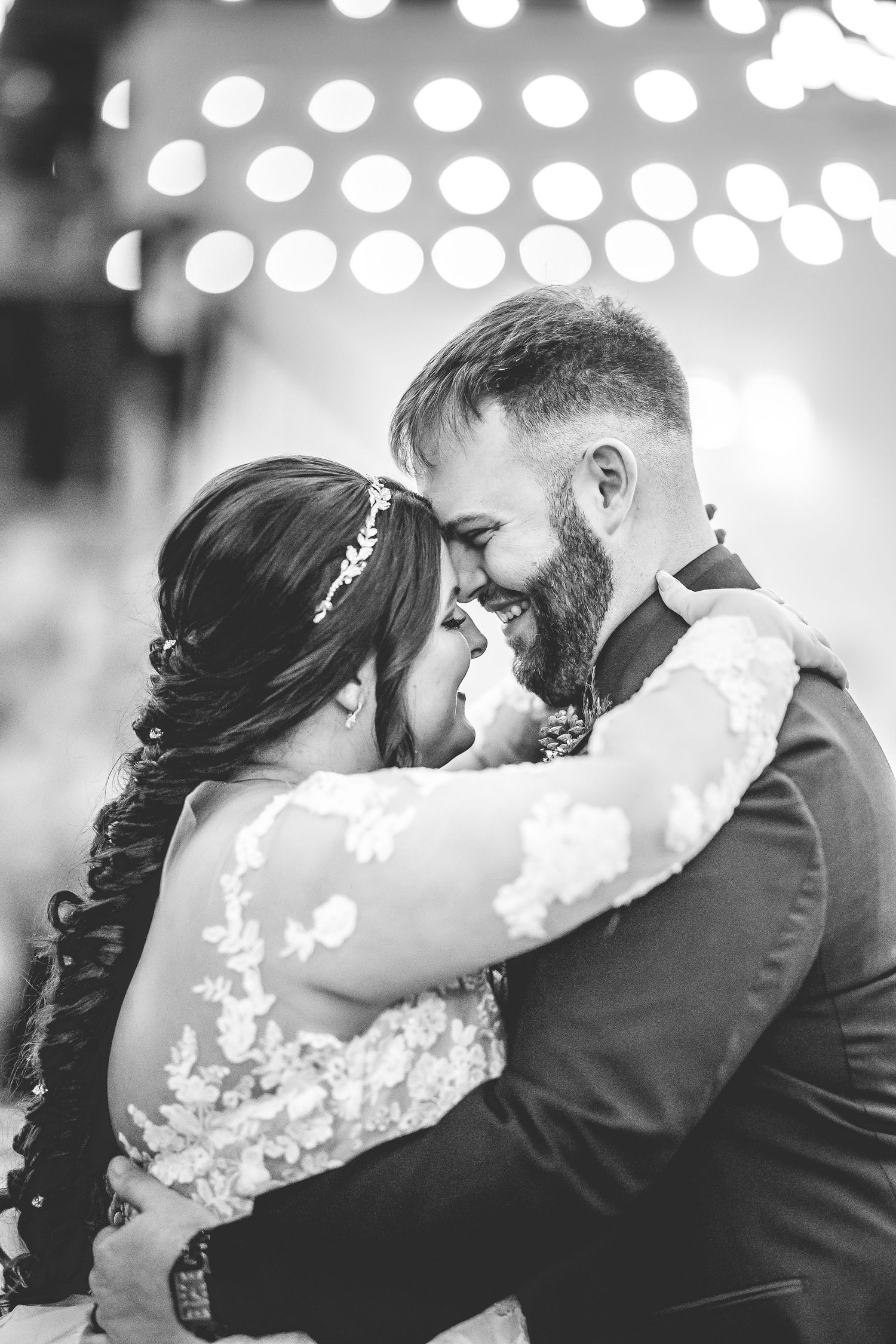 Intimate first dance moment captured under twinkling reception lights in black and white.