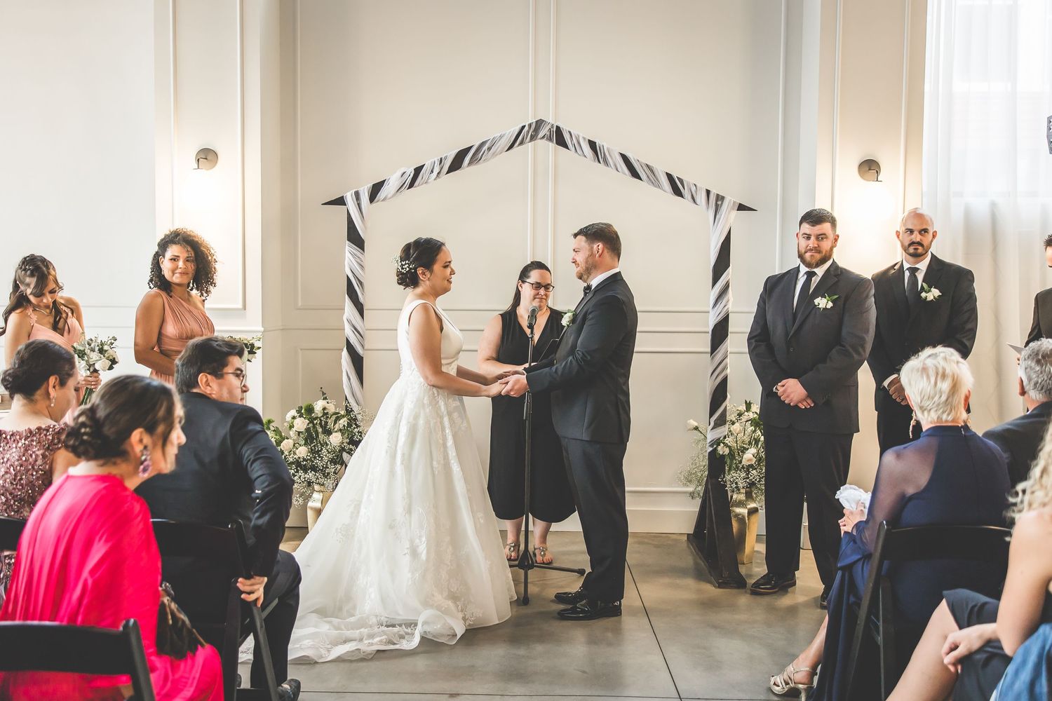 Wedding ceremony guests seated in a bright white venue with black and white striped decor elements.
