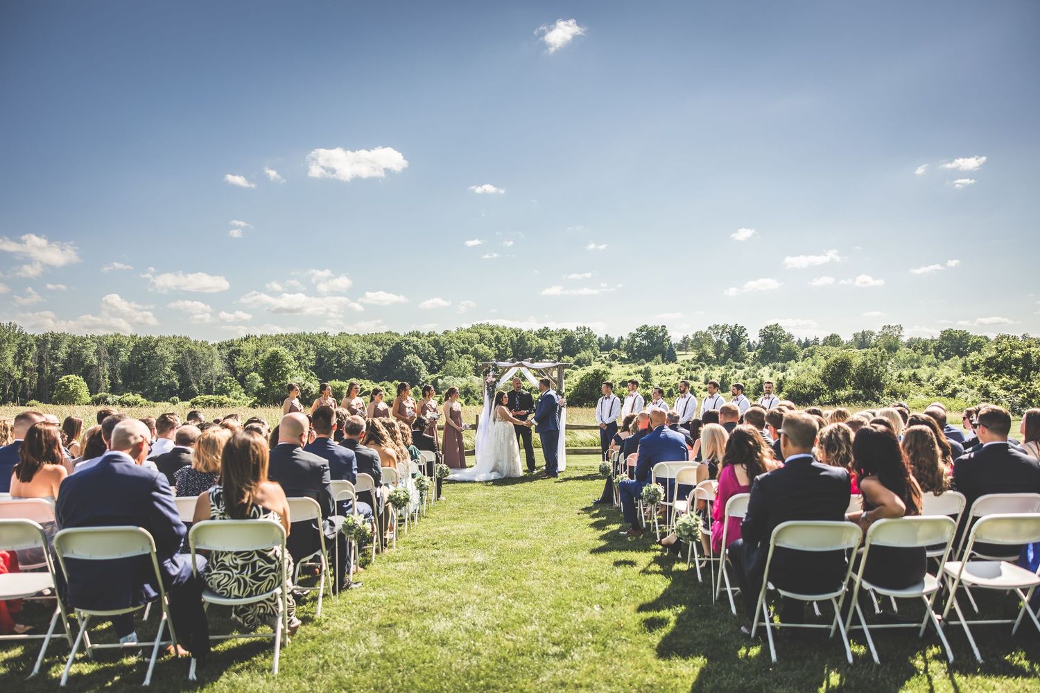 Panoramic view of outdoor wedding ceremony setup with rows of chairs in a grassy field.