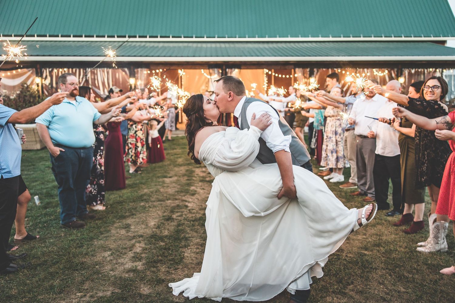 Wedding party dancing and celebrating outdoors under a green metal roof.