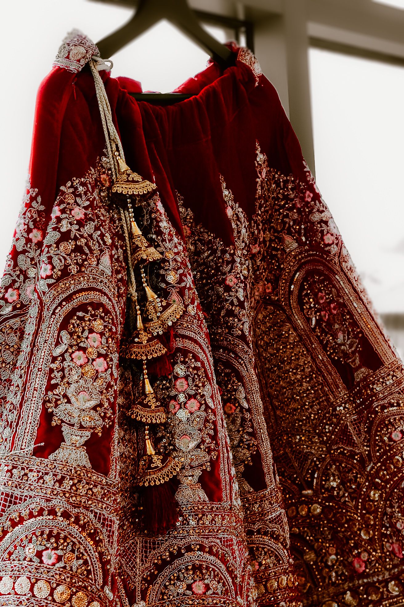 Ornate red wedding lehenga with intricate embroidery and beadwork details hanging on display.