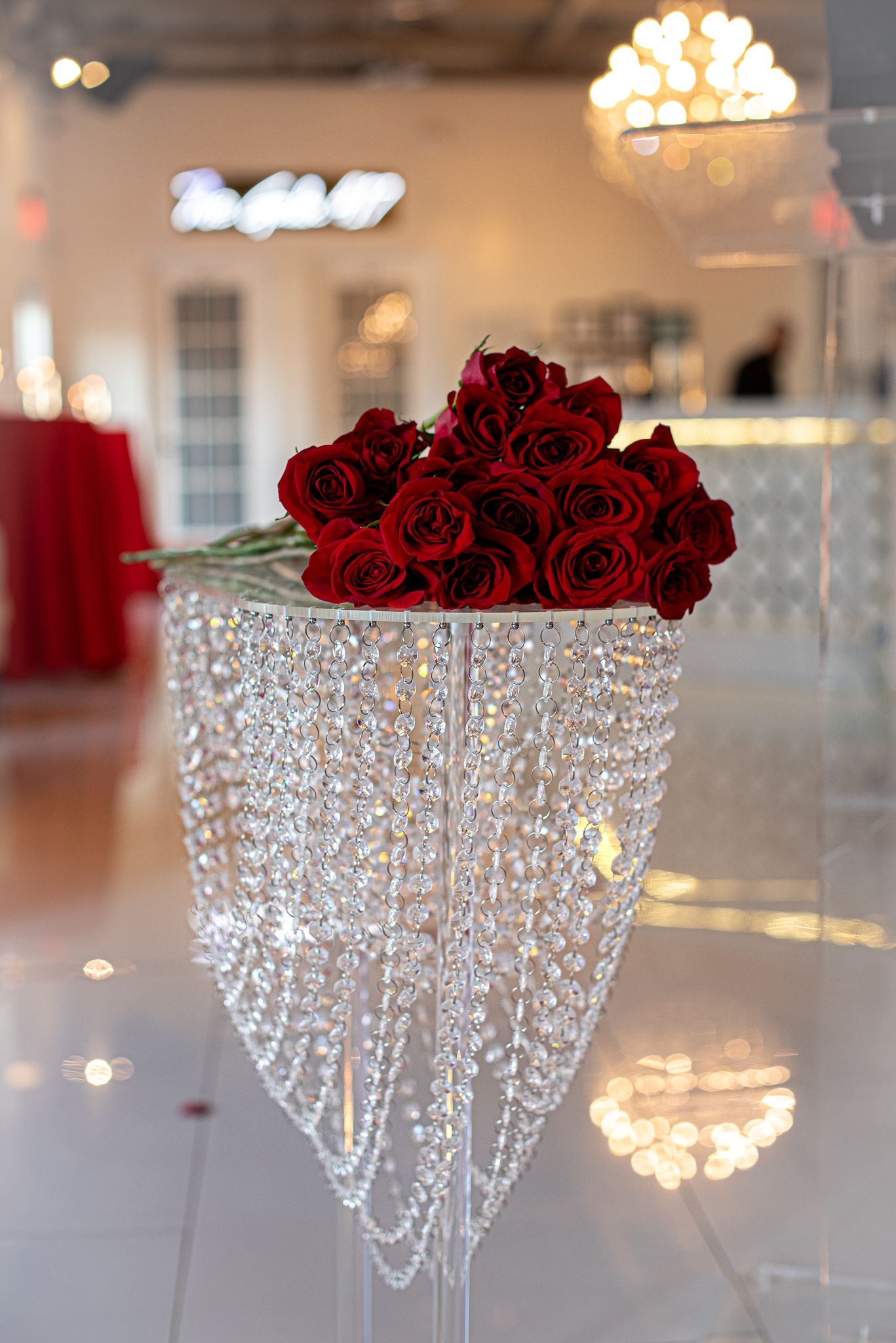 Crystal chandelier centerpiece adorned with red roses on white table.
