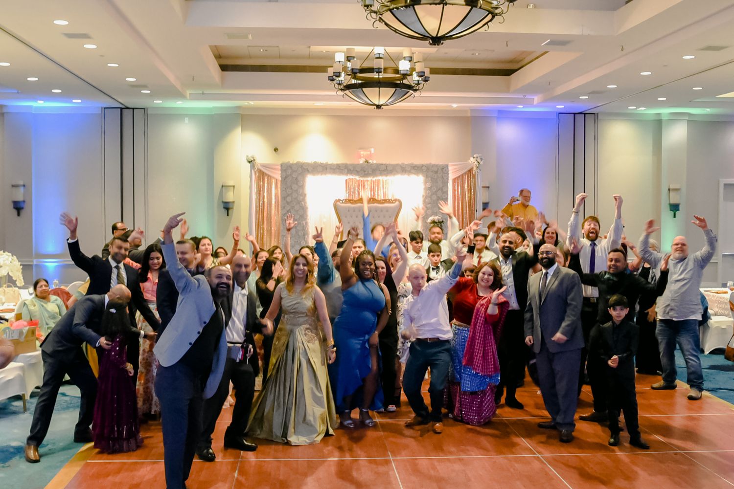 Large group celebration photo in elegant hotel ballroom with guests cheering.