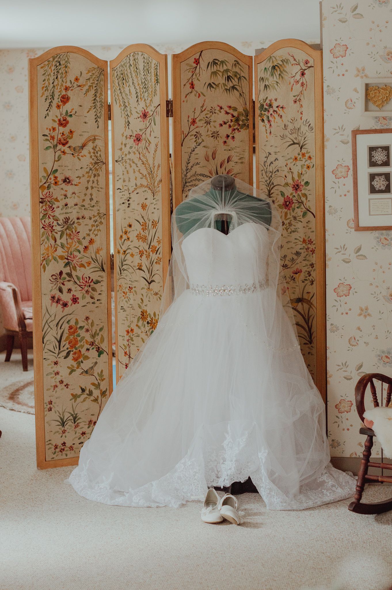 Elegant white wedding gown displayed against decorative folding screen with floral pattern.