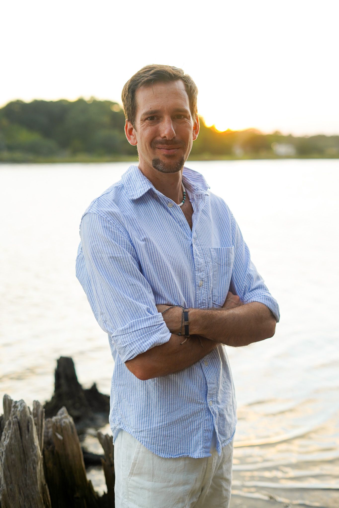 Person in striped shirt poses against waterfront backdrop during golden hour sunset.