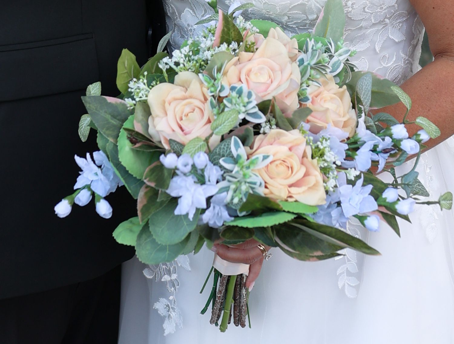 Bridal bouquet featuring peach roses, blue flowers, and greenery held against a black and white dress.