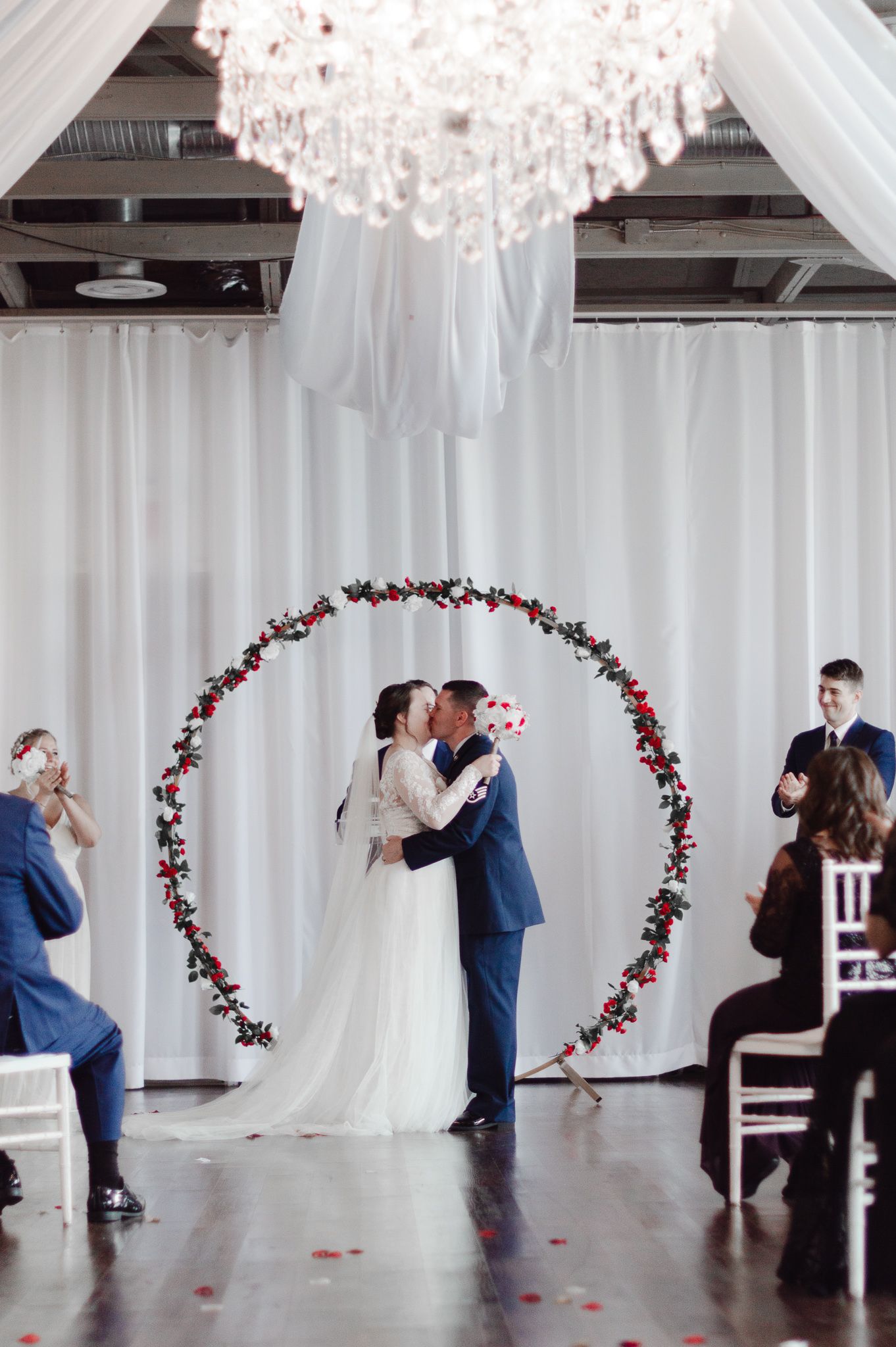 Wedding couple dances under floral arches and white draping in an elegant ballroom setting.