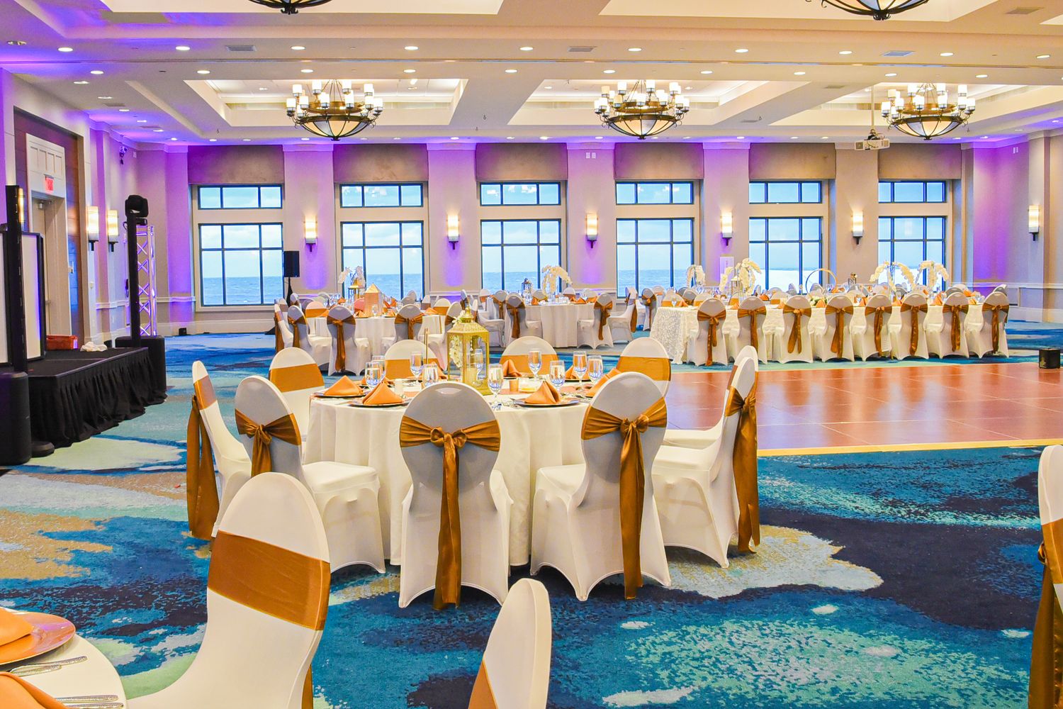 Luxurious banquet hall with purple lighting and white-covered chairs arranged in elegant table settings.