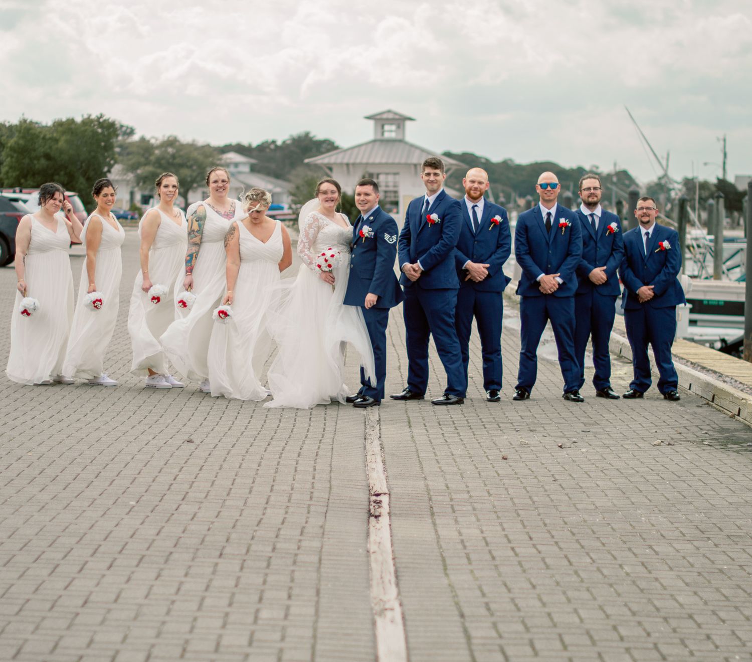 Wedding party in navy suits and white dresses posed along waterfront walkway.