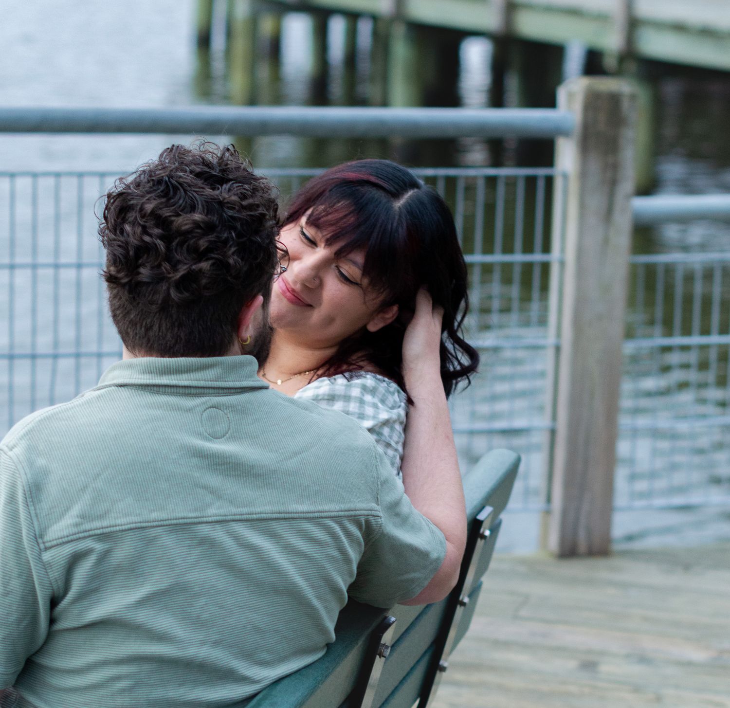 Couple sitting on a bench by a waterfront dock, sharing an intimate moment outdoors.