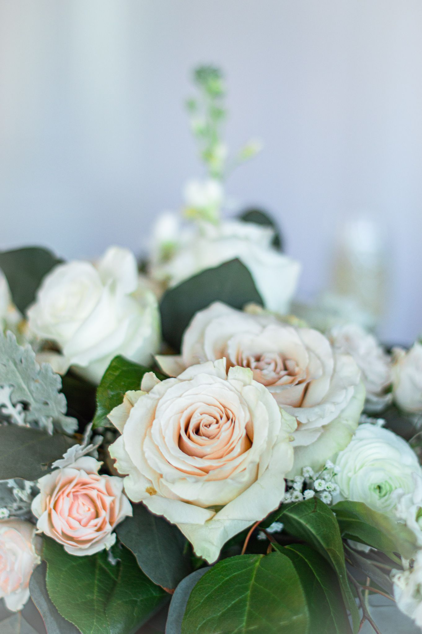 Delicate arrangement of blush roses and white flowers with green foliage.