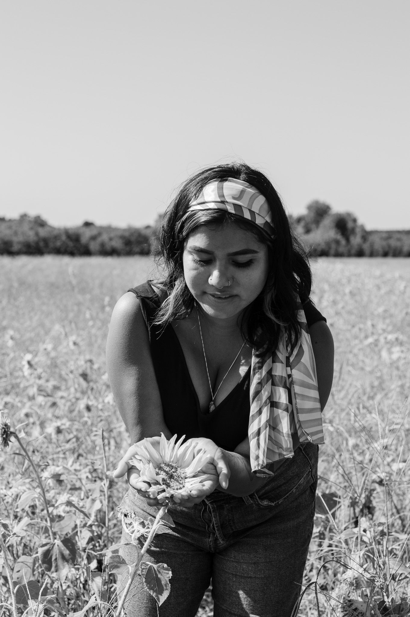 A person in a bandana examines flowers in a sunny field.
