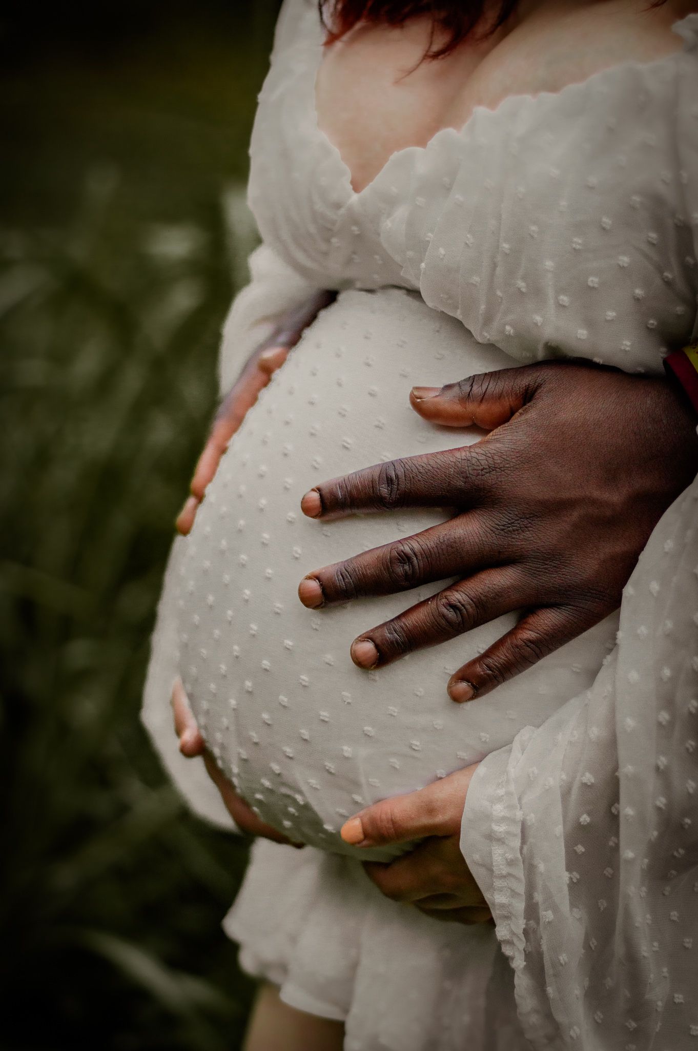 Close-up of hands cradling a pregnant belly in a textured white maternity dress.
