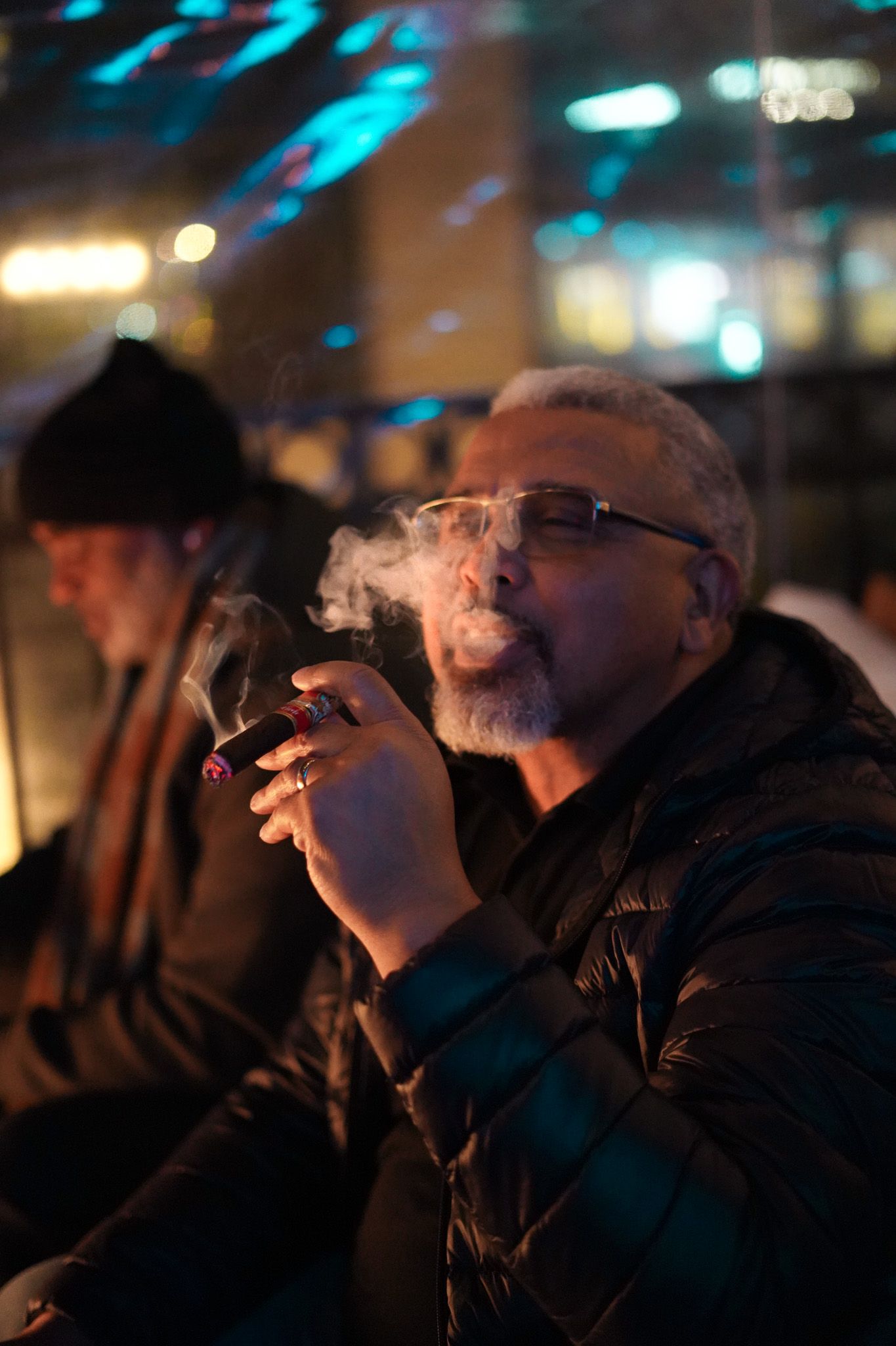 Silhouette of a person smoking a cigar in a dark room with blue lighting effects in the background.