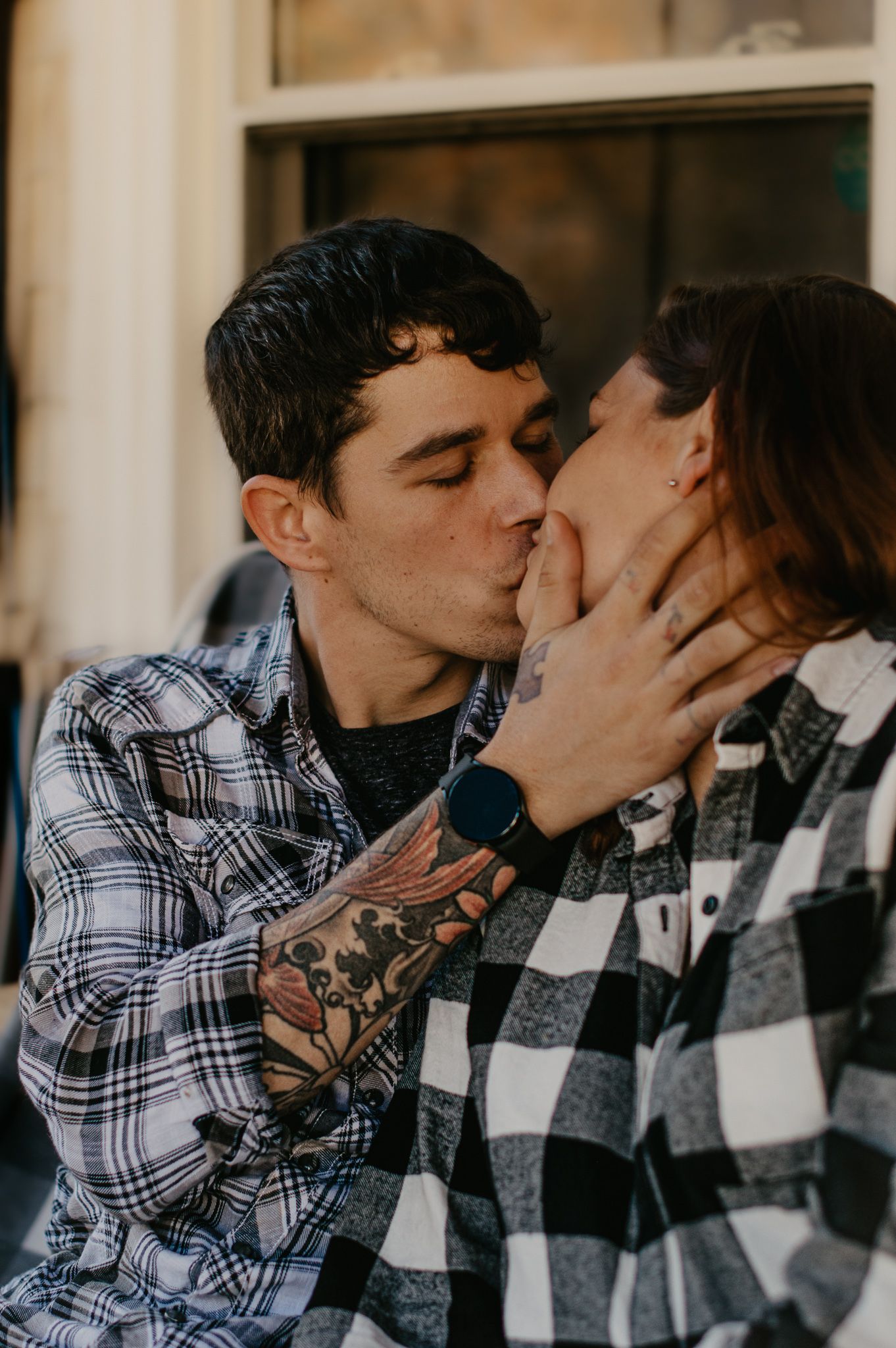 Intimate couple sharing tender kisses while wearing plaid shirts.