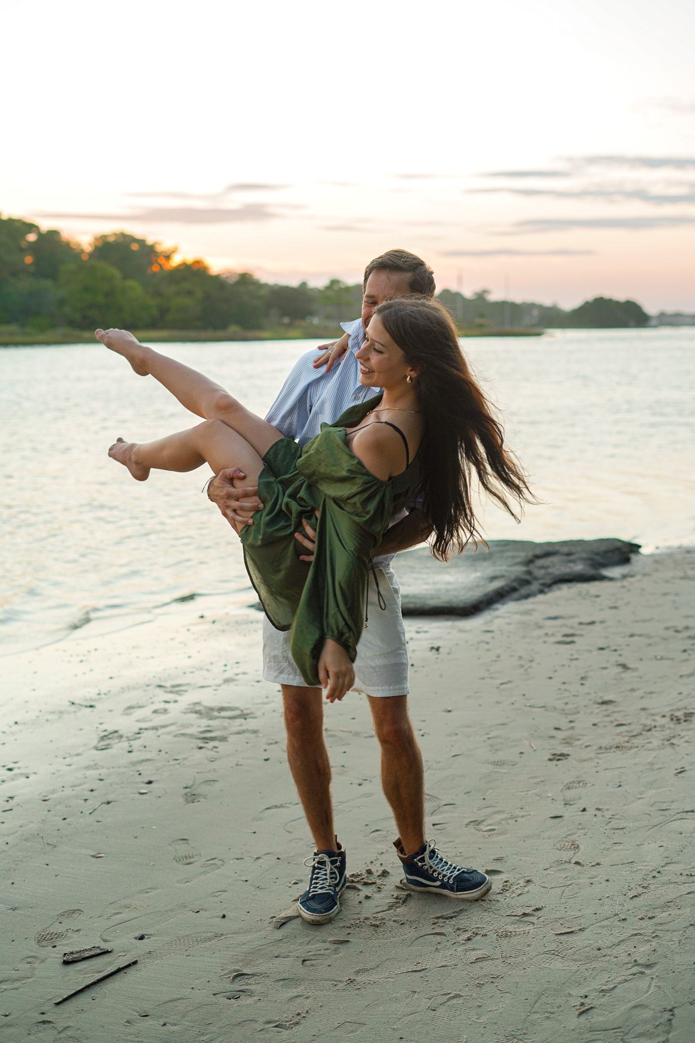 Playful couple dances on the beach at sunset with dramatic dip pose.