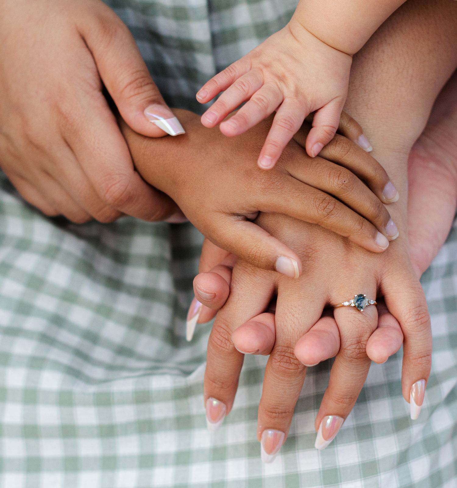 Three generations of family hands stacked together, featuring French manicured nails and a diamond engagement ring.