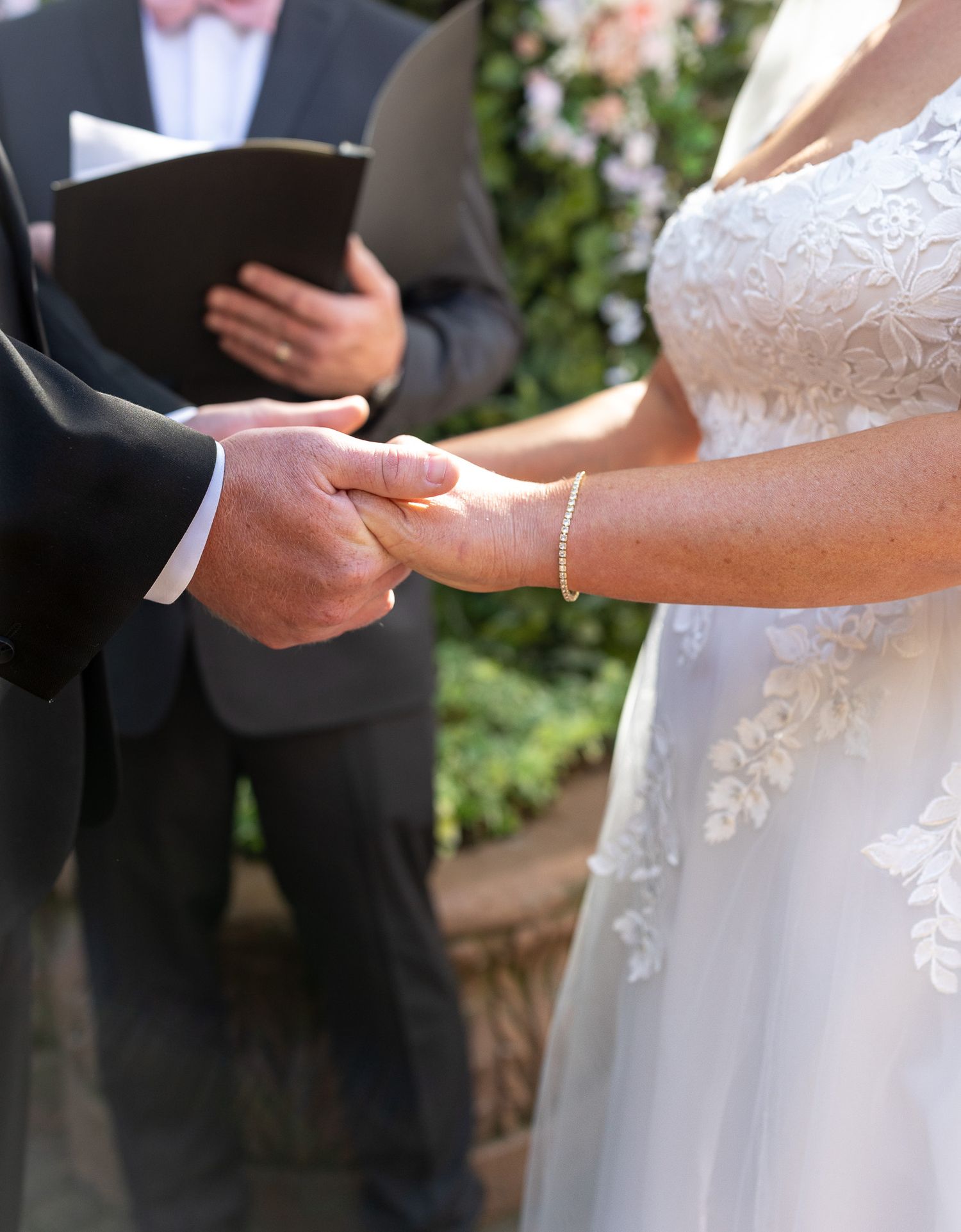 Bride and groom exchanging rings during outdoor wedding ceremony with officiant holding book in background.