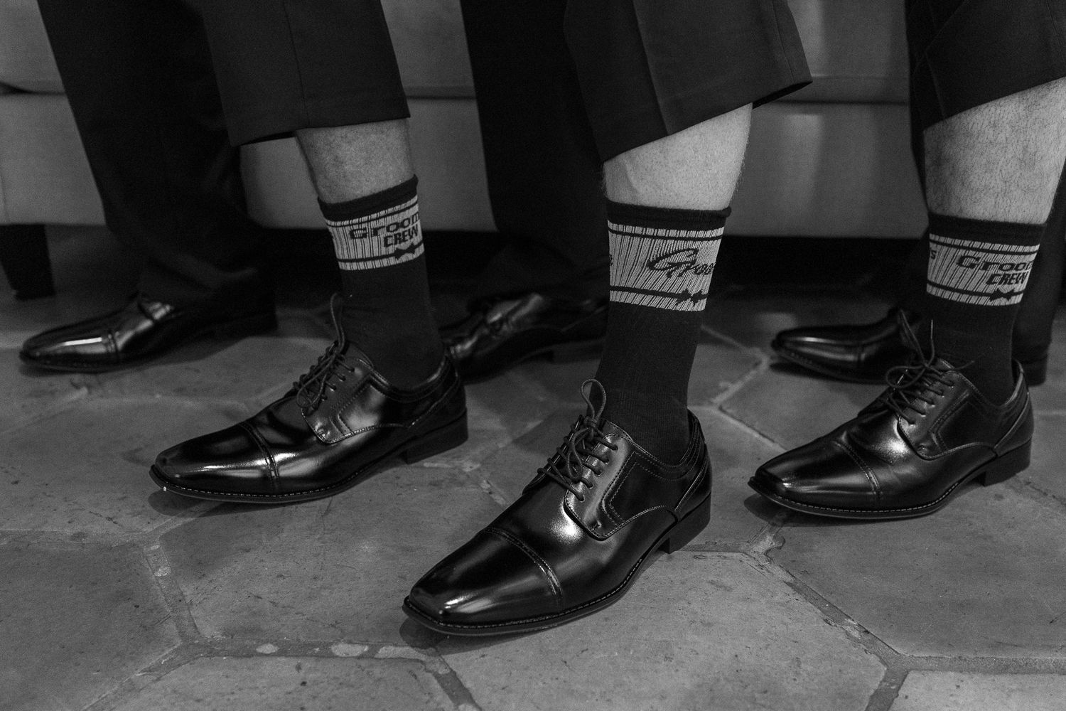 Black and white photo of men wearing dress shoes and patterned socks on a stone floor.