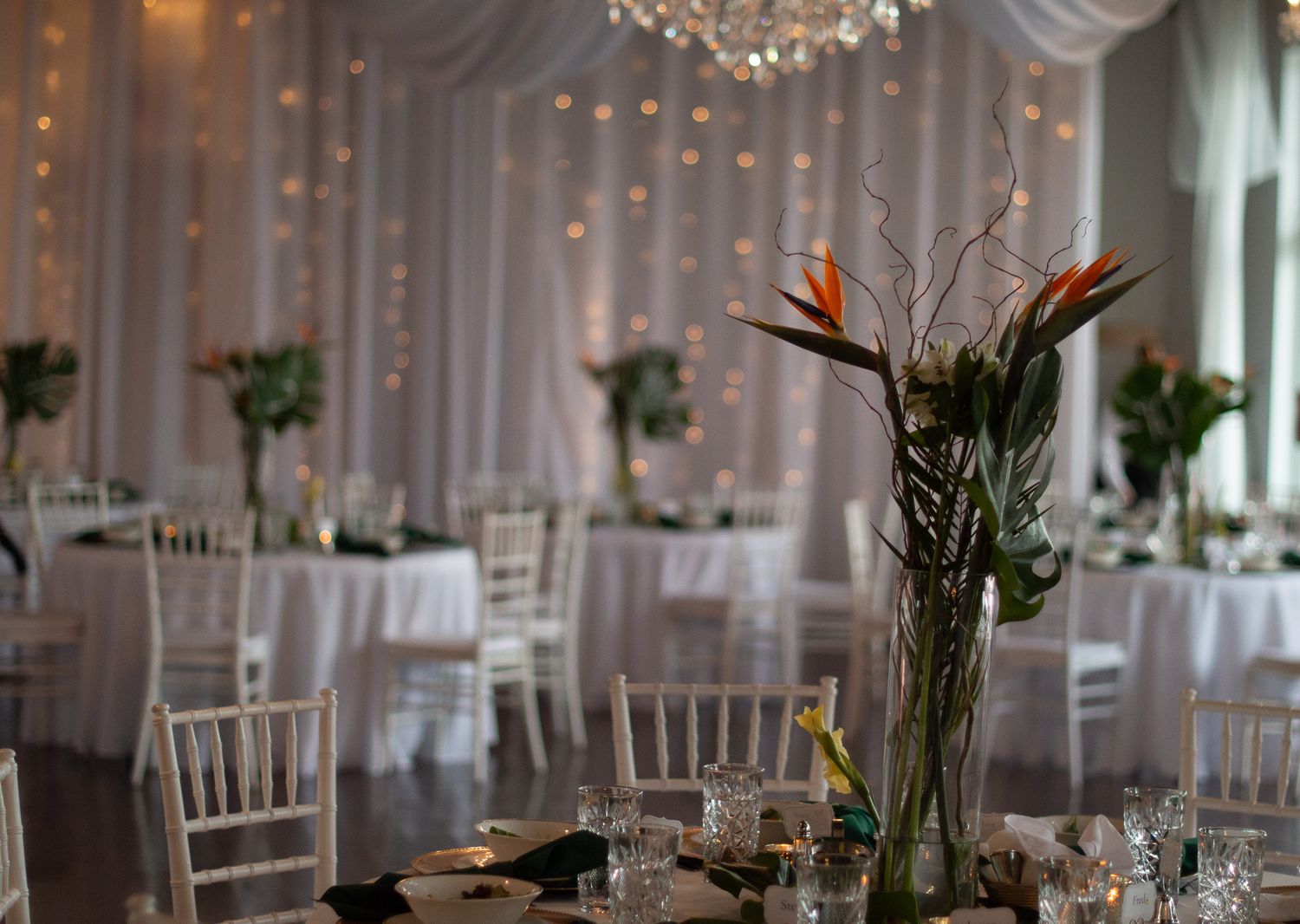 Wedding reception tables set with elegant centerpieces under crystal chandeliers and white draping.