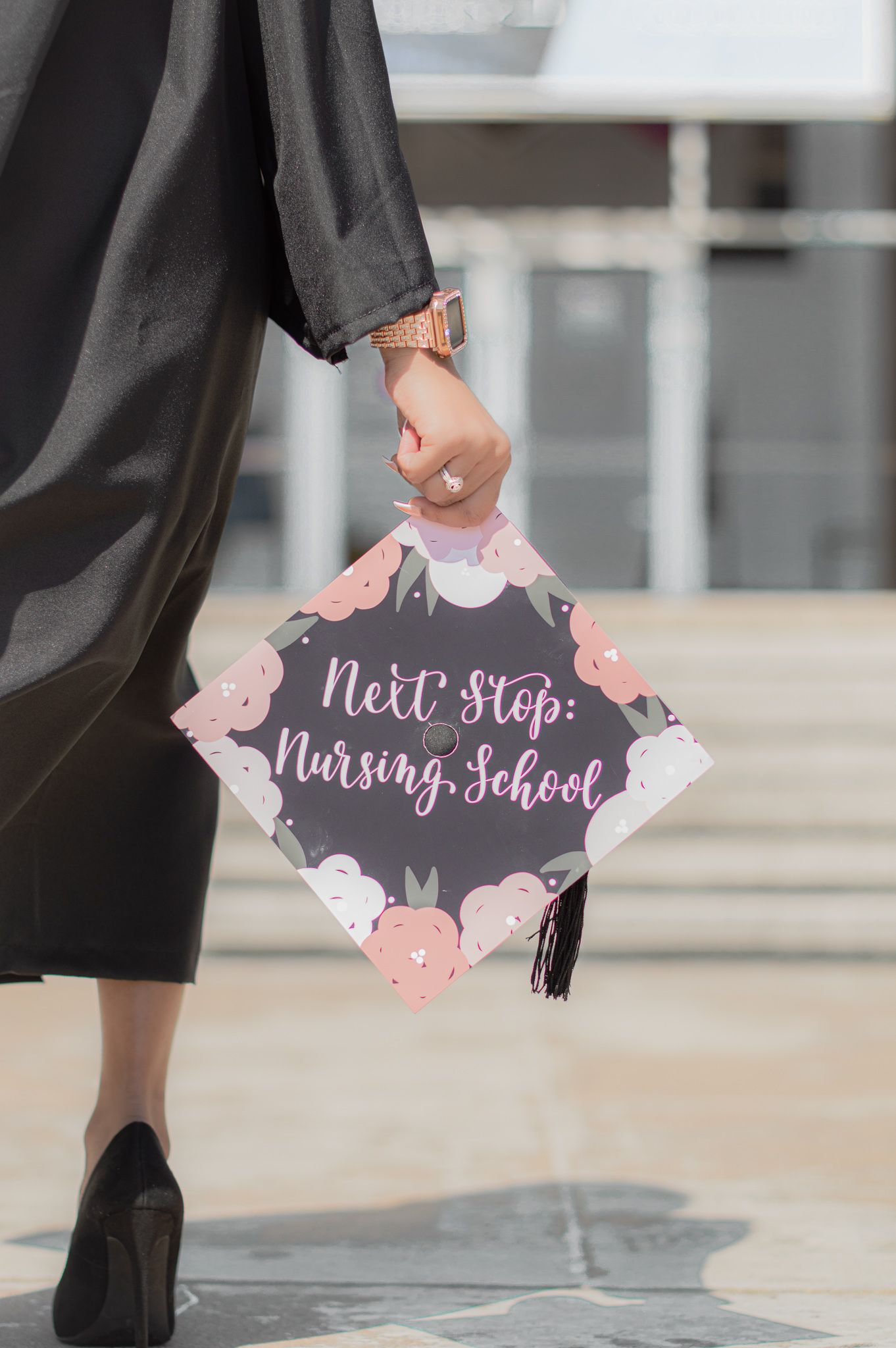A series of graduation cap decorations with pink floral designs and text about nursing school shown against a concrete floor.