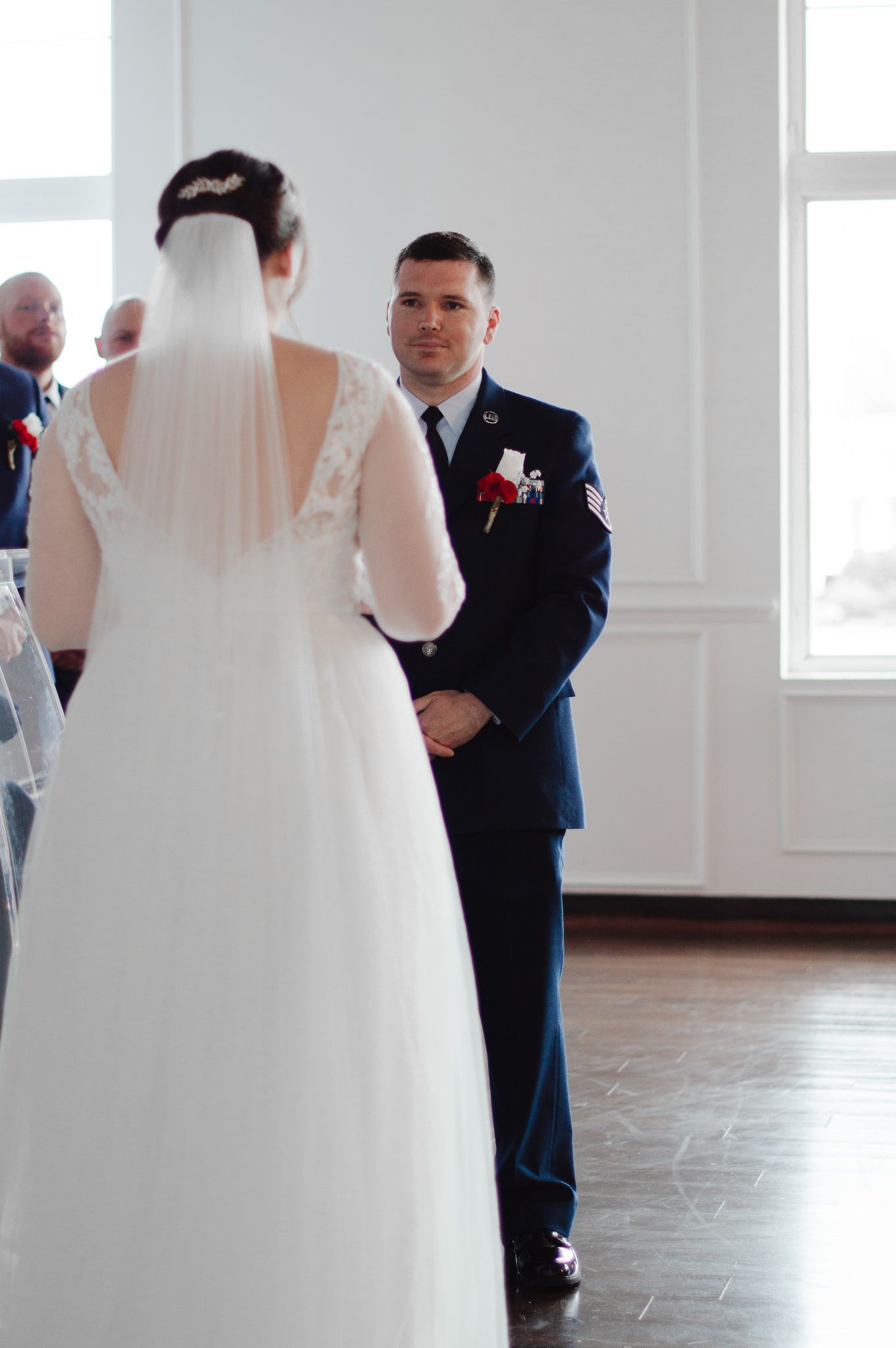 A couple shares their first dance in an elegant white ballroom with large windows.