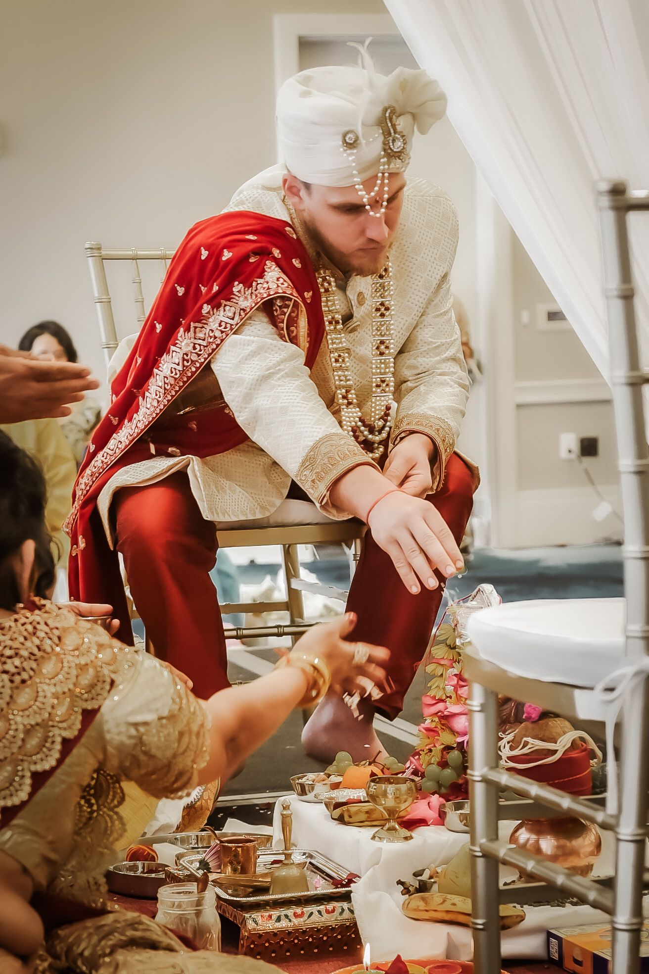Traditional Indian groom in white and red attire participating in wedding ceremony rituals.