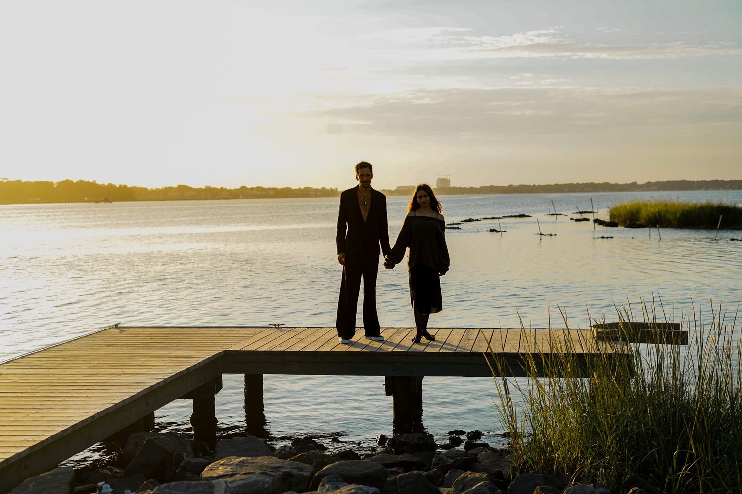 Silhouettes of a couple standing together against a waterfront sunset.
