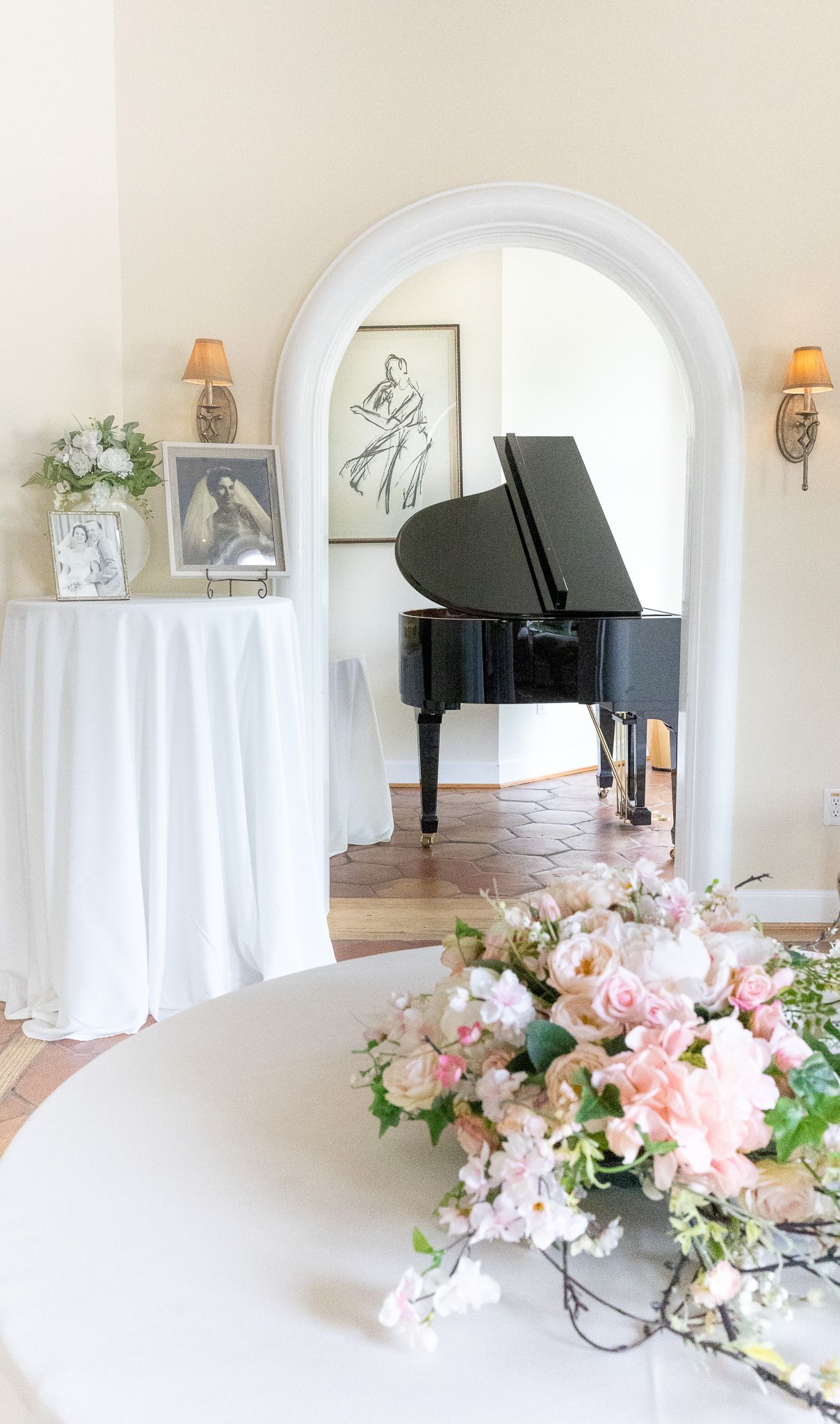 Elegant wedding venue with black grand piano, floral arrangements, and white draped table under a classic arch.