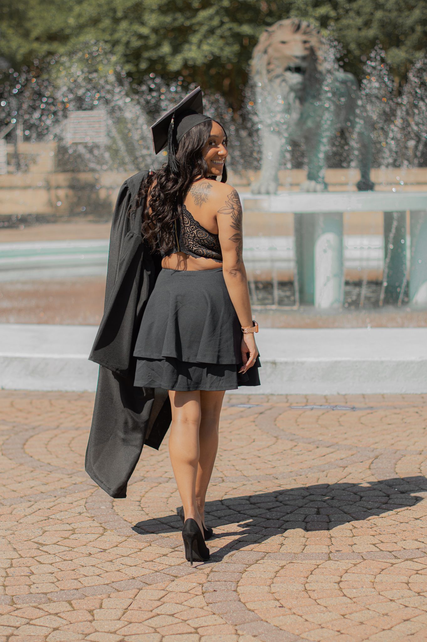 Black graduation gown flowing on brick pavement during outdoor photoshoot.