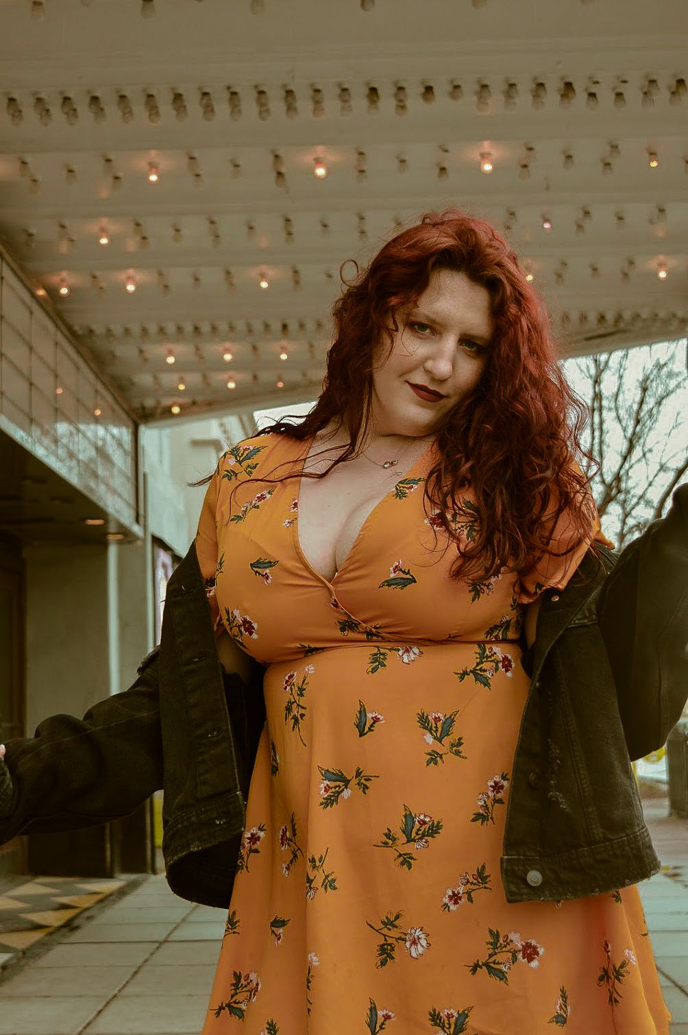 Portrait in warm lighting showing person wearing orange floral top under string lights.