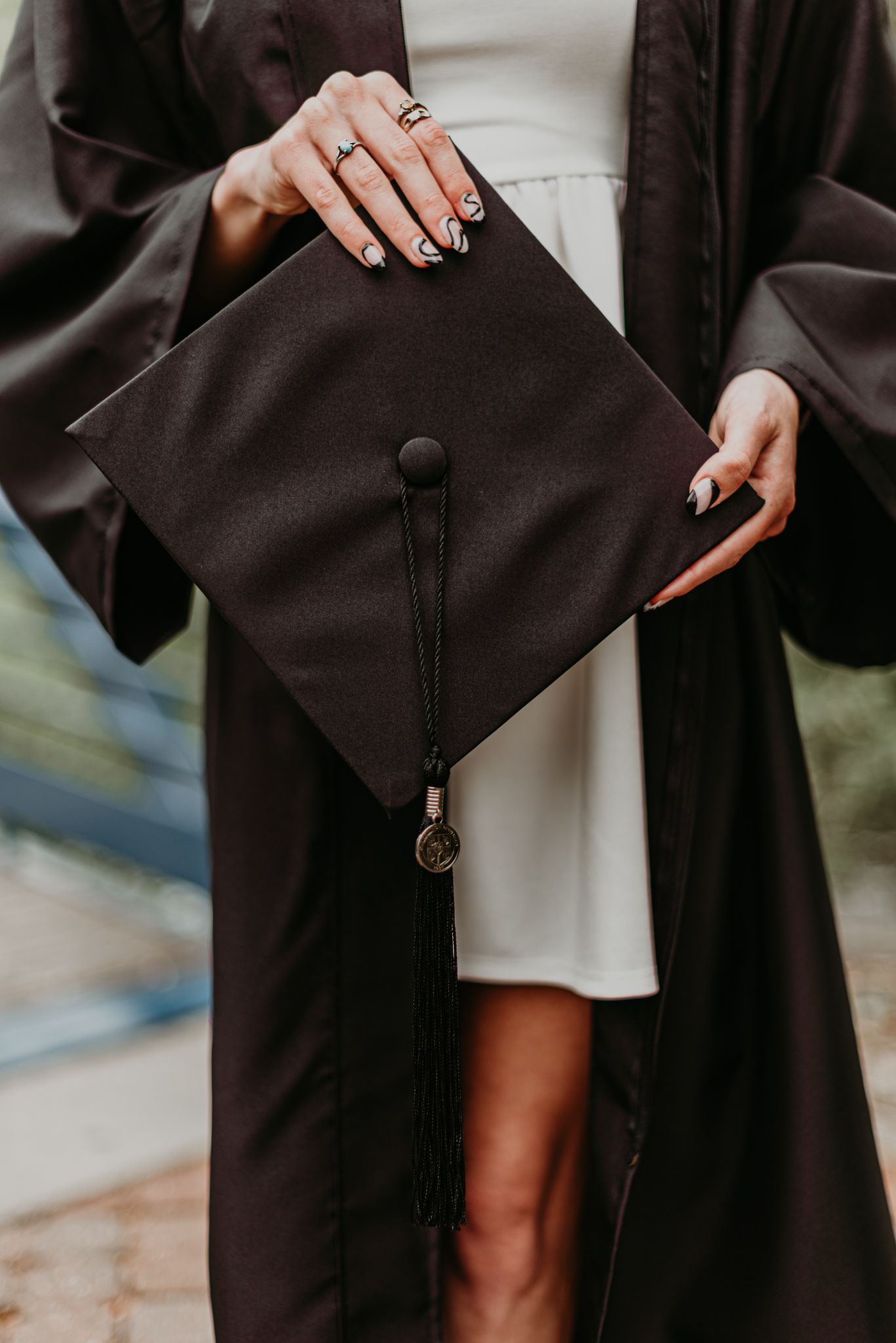 Detail shot of hands holding graduation gown against white dress.