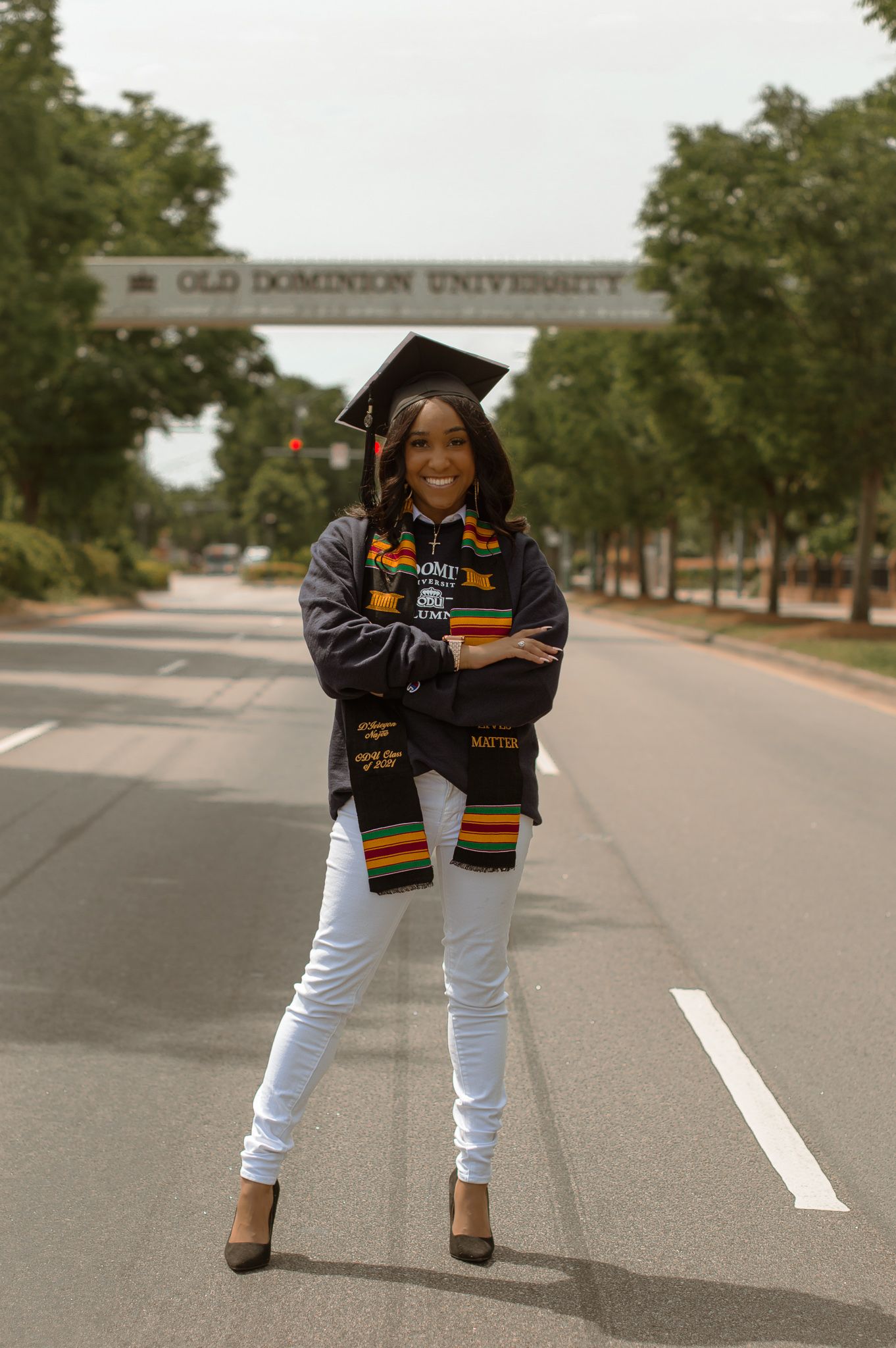 Graduate poses in white pants and decorated graduation stole on campus street at Old Dominion University.
