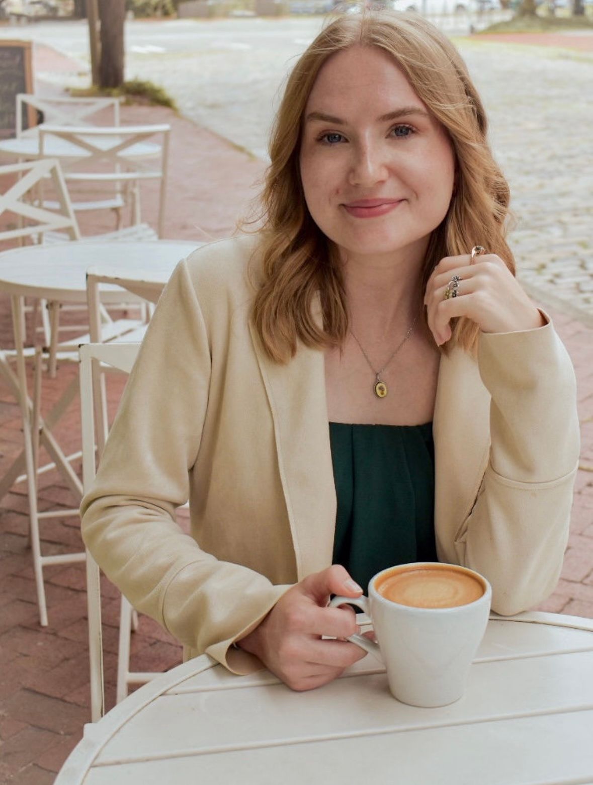 Person enjoying coffee at an outdoor cafe with cream colored blazer.