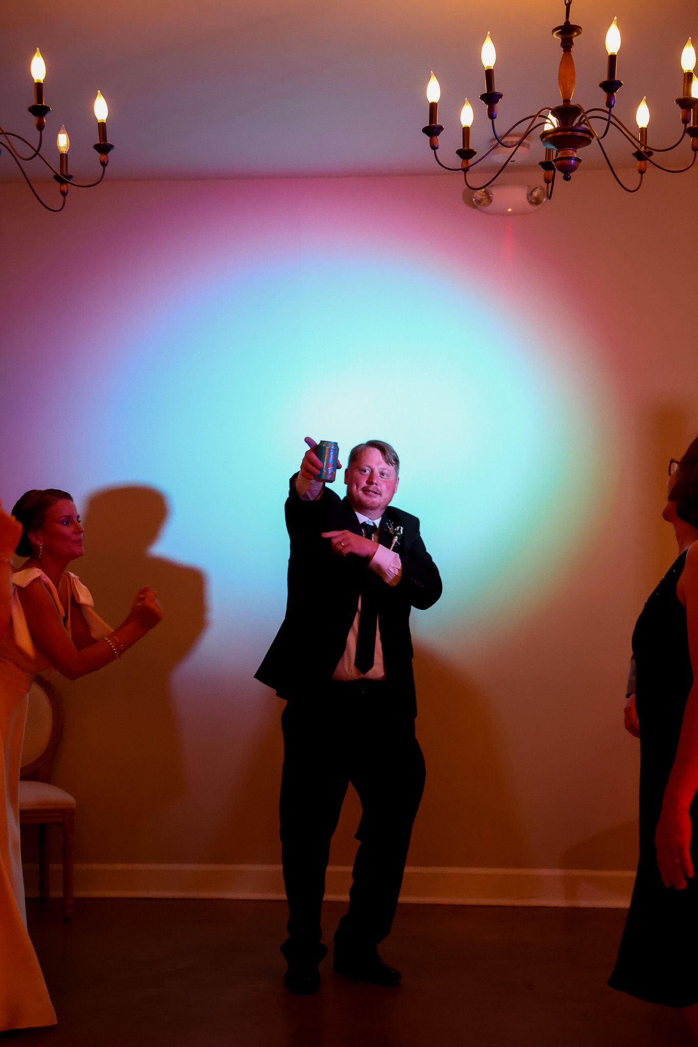 Man in suit takes selfie on dance floor with colorful lights and chandelier at formal event.