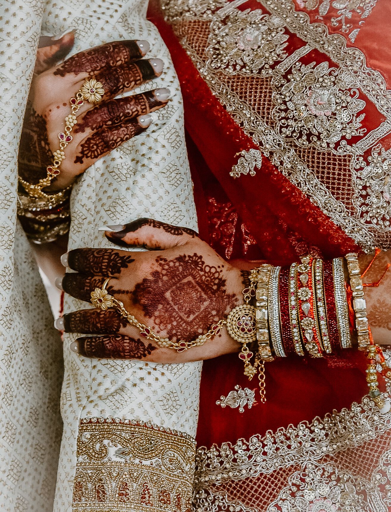 Close-up of traditional Indian bridal hands with henna and bangles against red and white fabric.