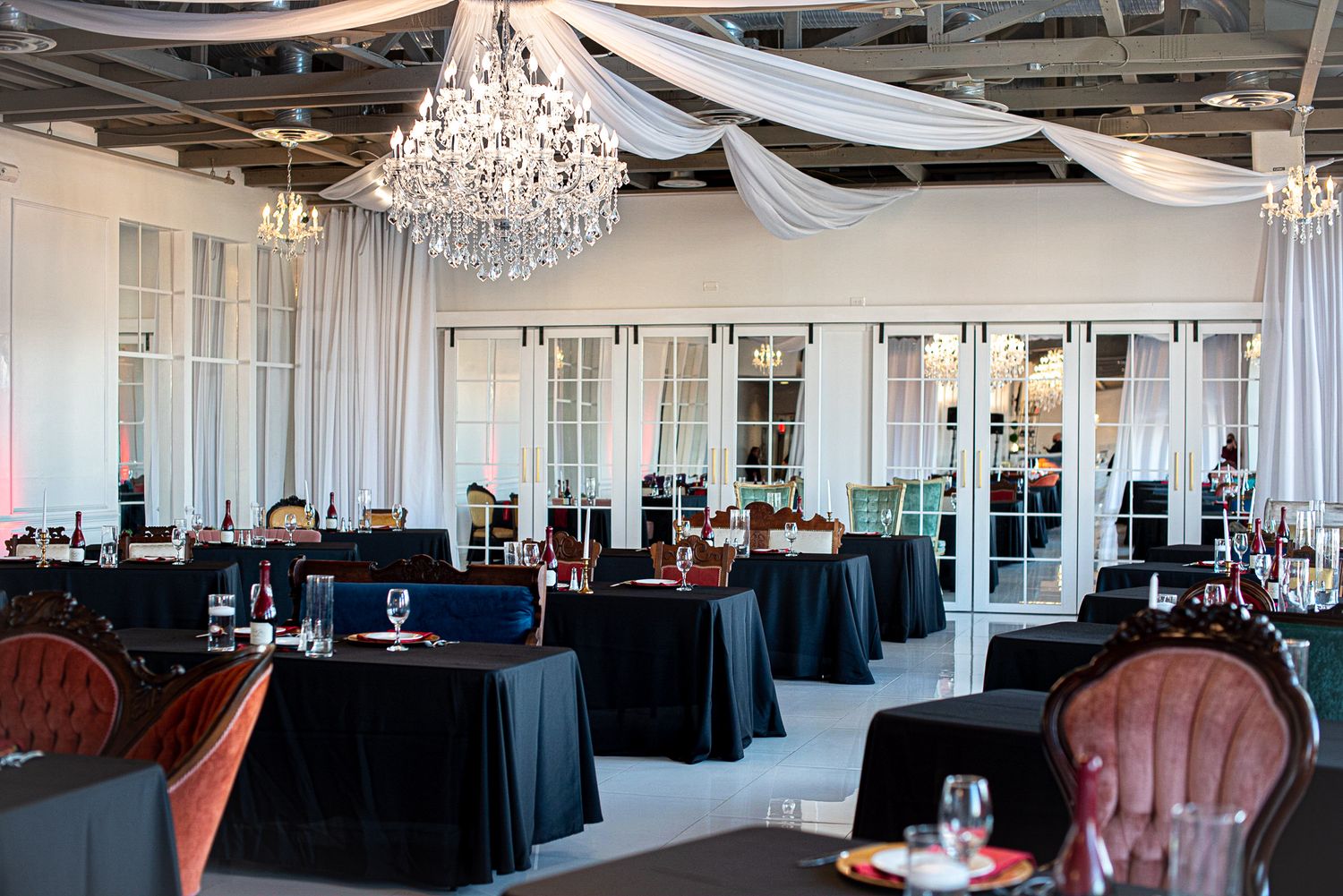 Spacious wedding reception venue with black linens and crystal chandeliers.