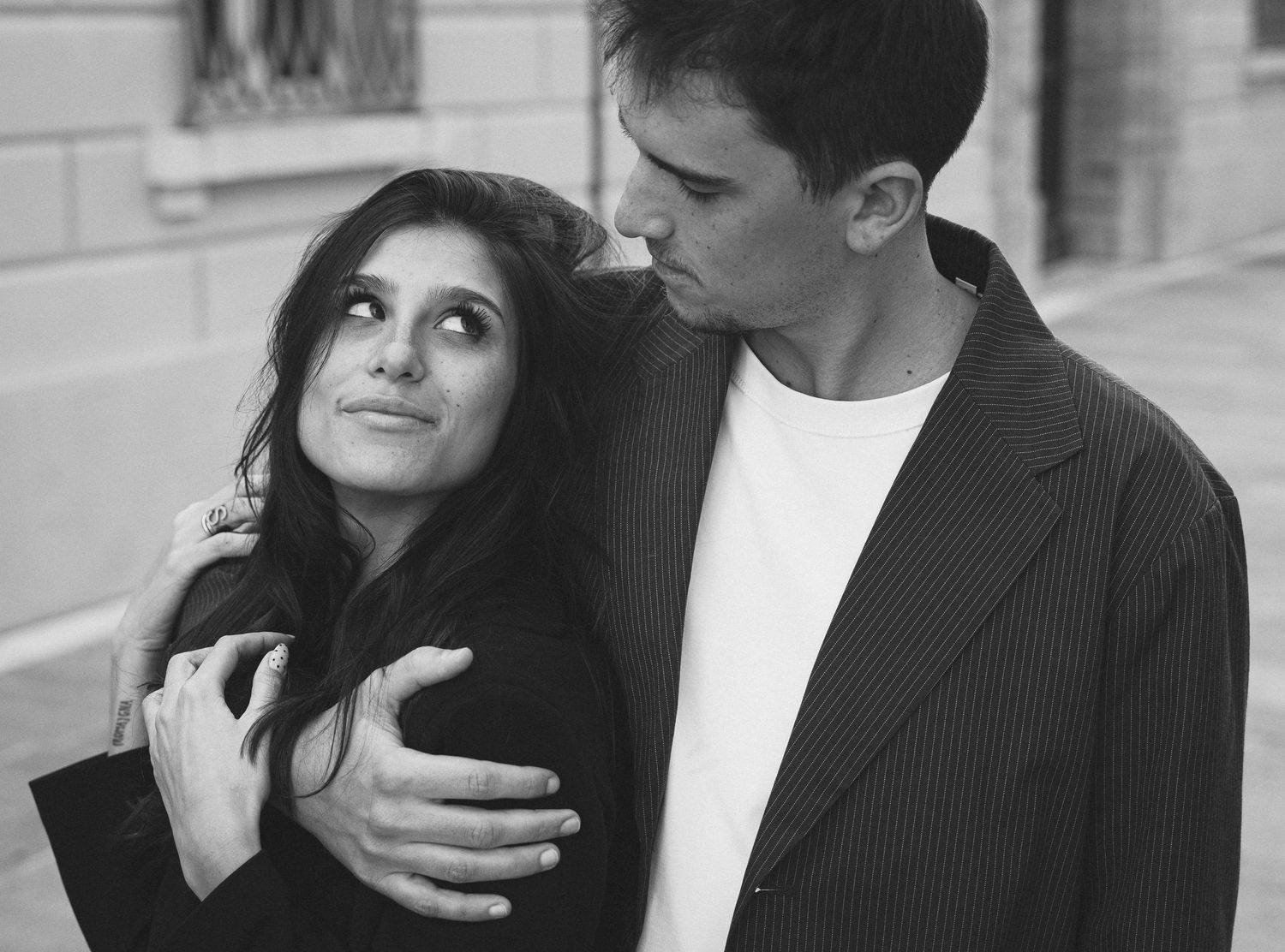 Black and white photo of a young couple embracing outdoors, woman looking up at man affectionately.