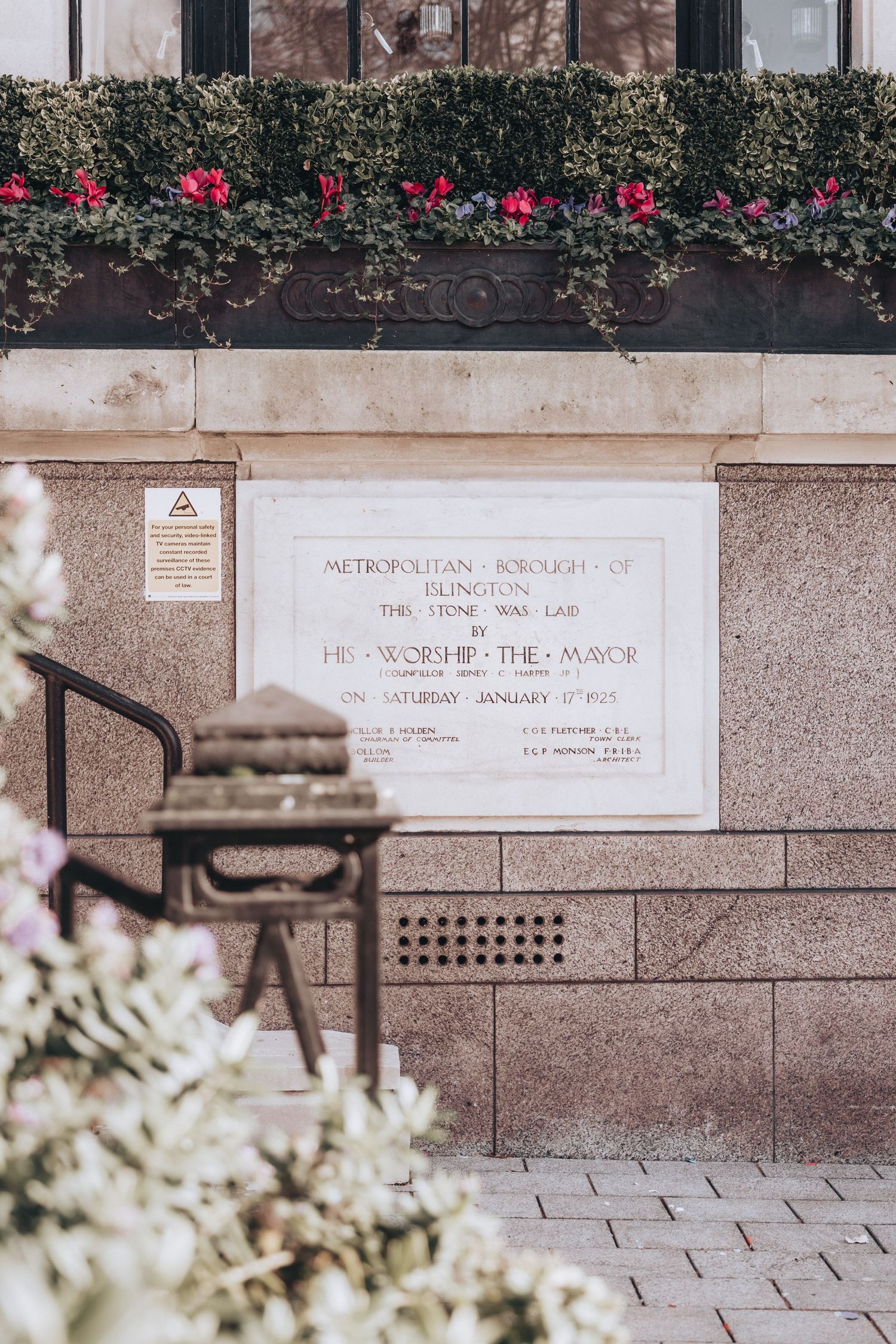 Historic Metropolitan Borough of Islington foundation stone plaque on a granite wall with flowers above.