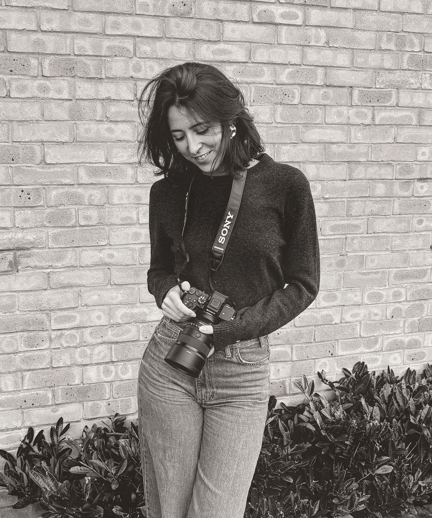 Candid shot of a wedding photographer in black jacket and jeans against brick wall background.