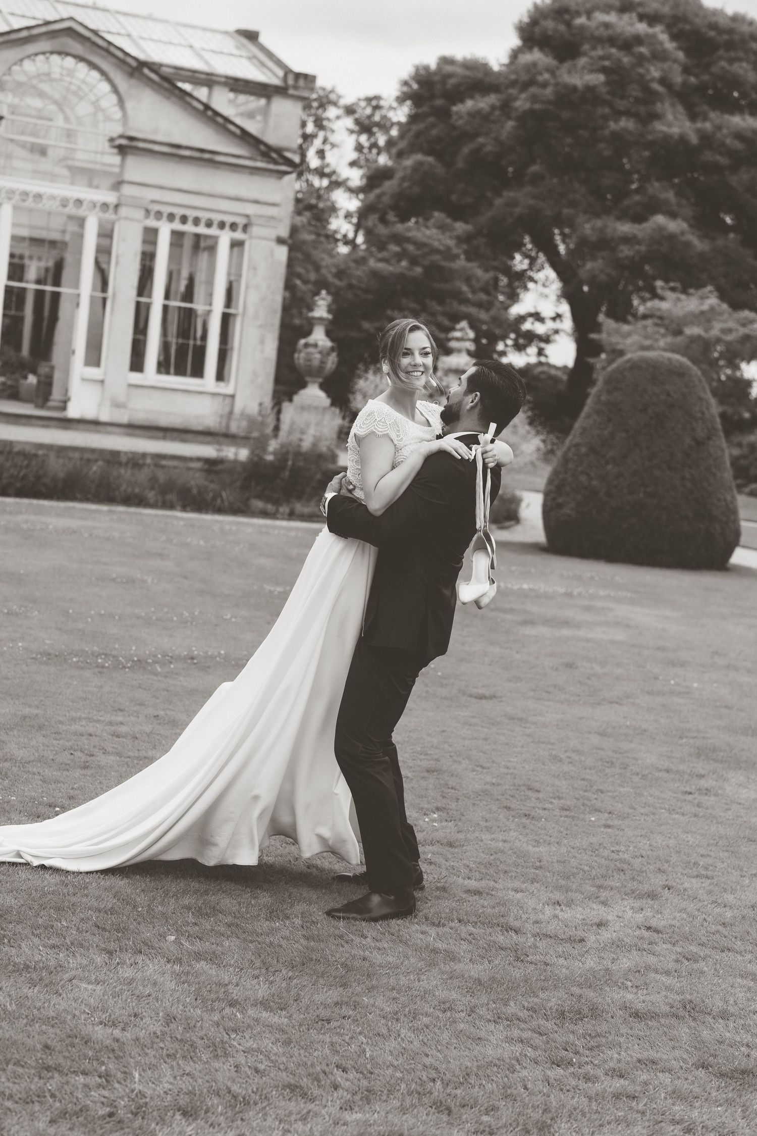 Groom lifting bride in wedding dress on Syon Park estate lawn in black and white photo.