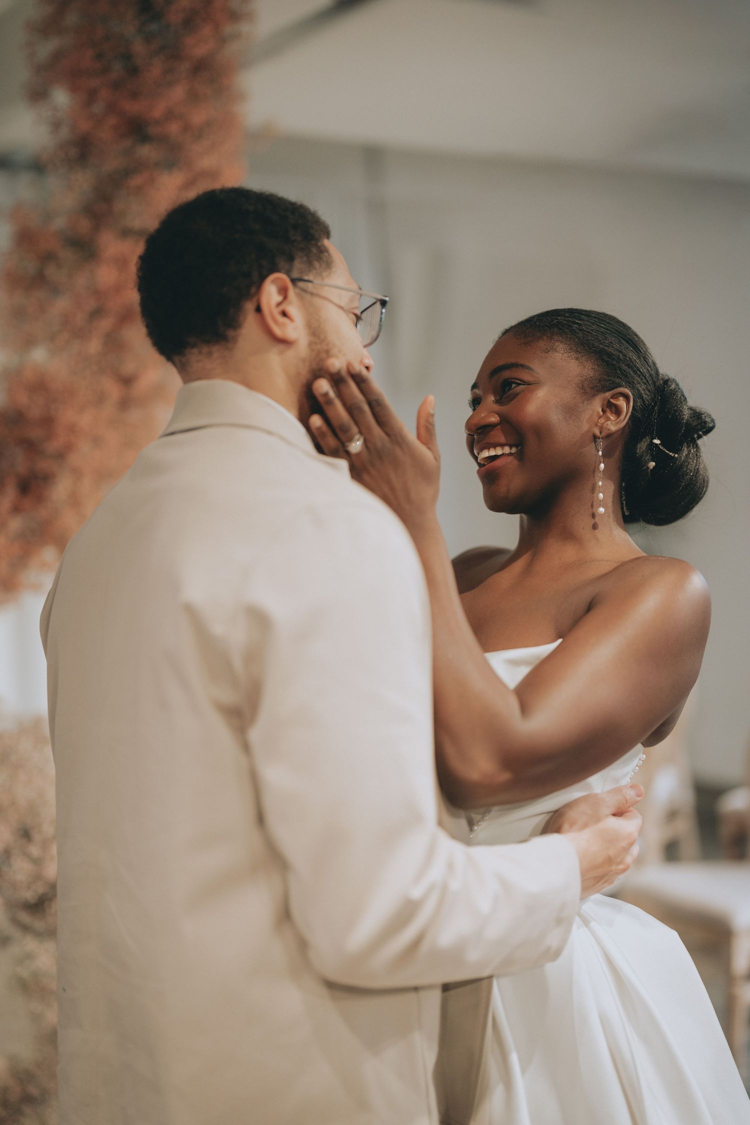A joyful Black bride in a white strapless gown touches her groom's face during their wedding dance.