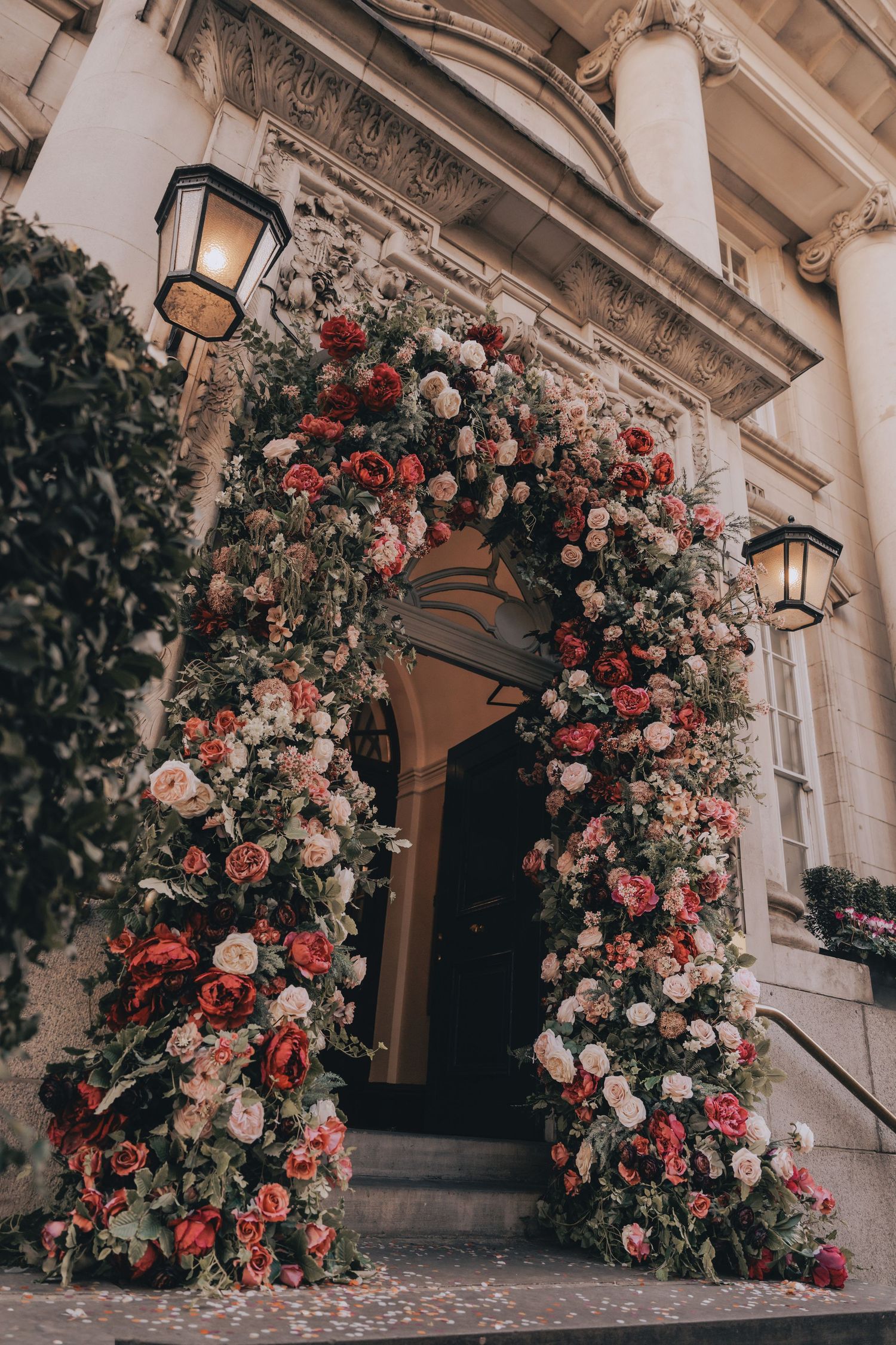Elegant floral arch of Chelsea Old Town Hall adorned with red and pink roses framing a grand building entrance with ornate stone columns.