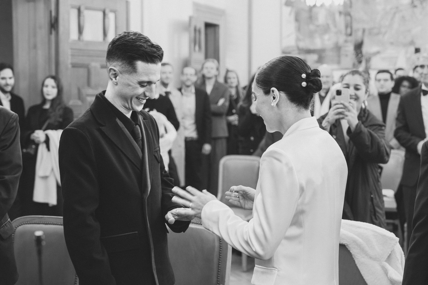Black and white wedding ceremony photo of bride and groom exchanging rings before guests in Lille town hall in France.