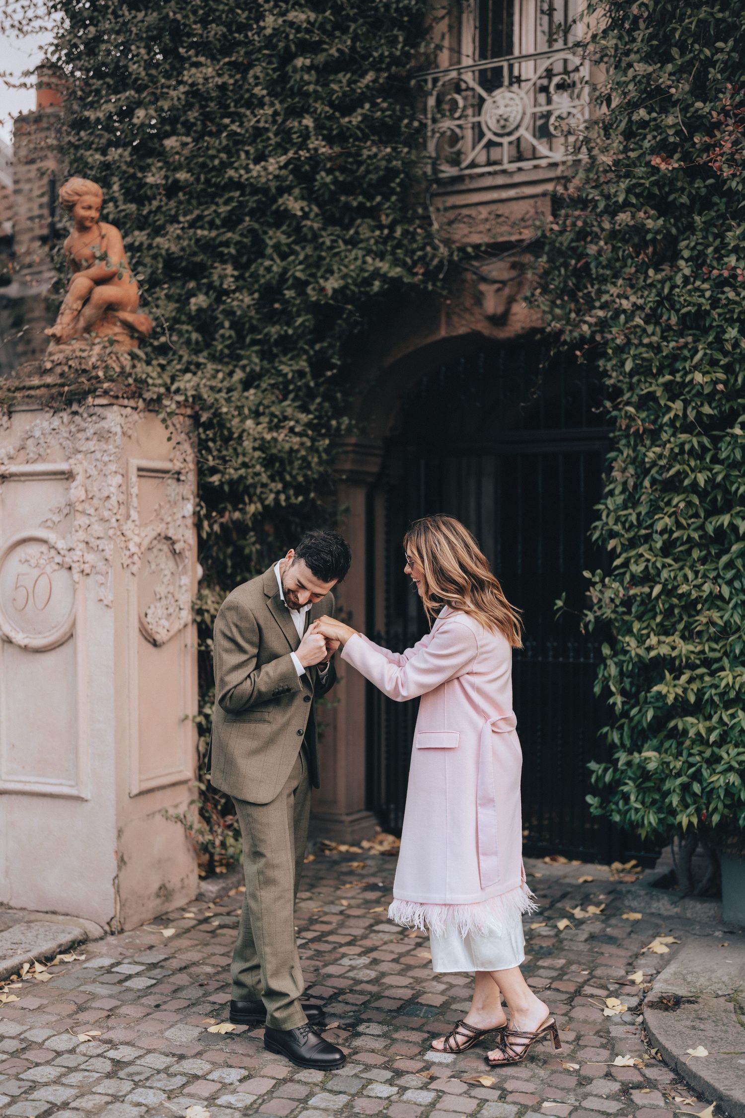 Elegant couple holding hands outside an ivy-covered historic building on cobblestone street in Chelsea near Chelsea Old Town Hall.