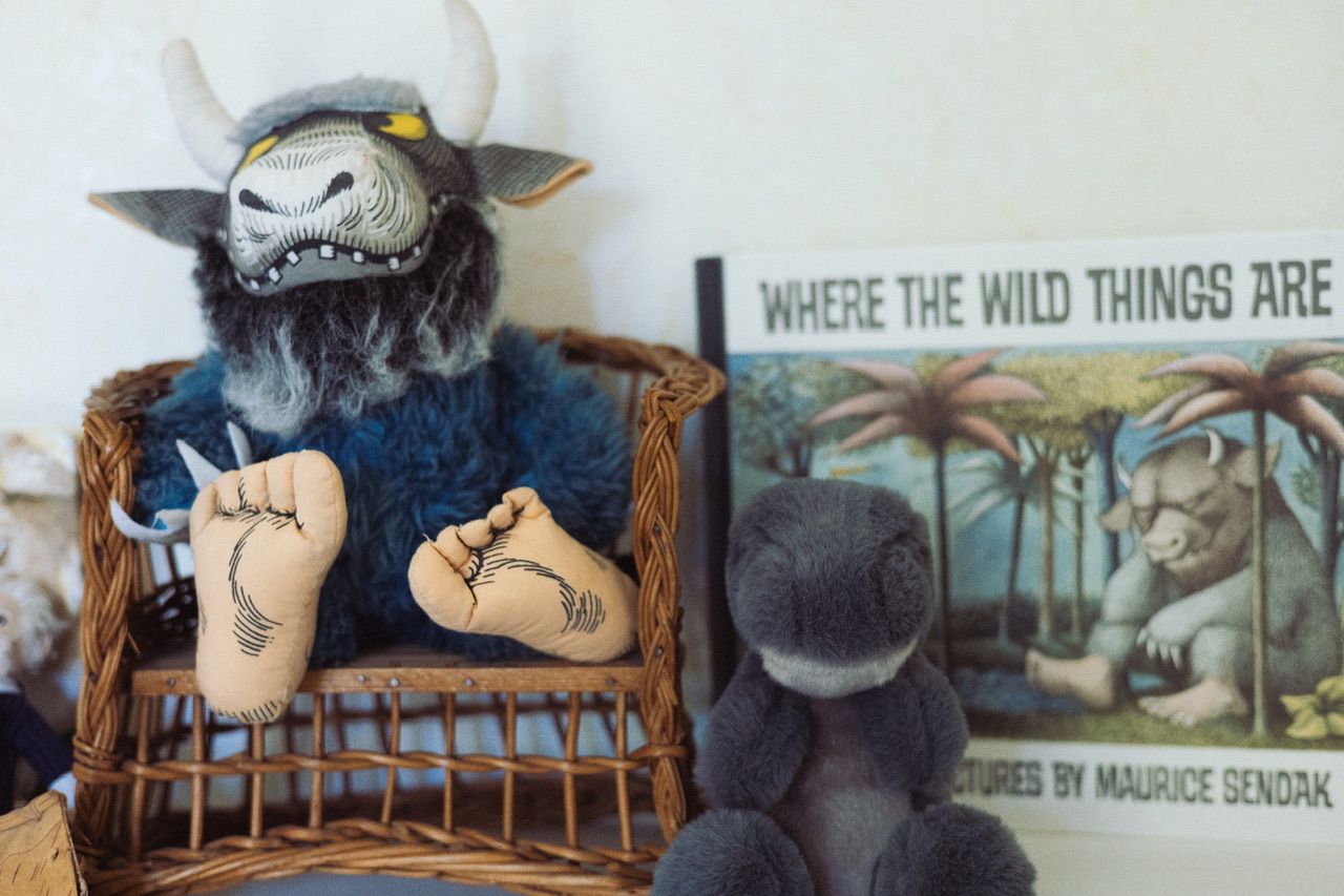 Plush toys and children's books including Where the Wild Things Are displayed on a nursery shelf.