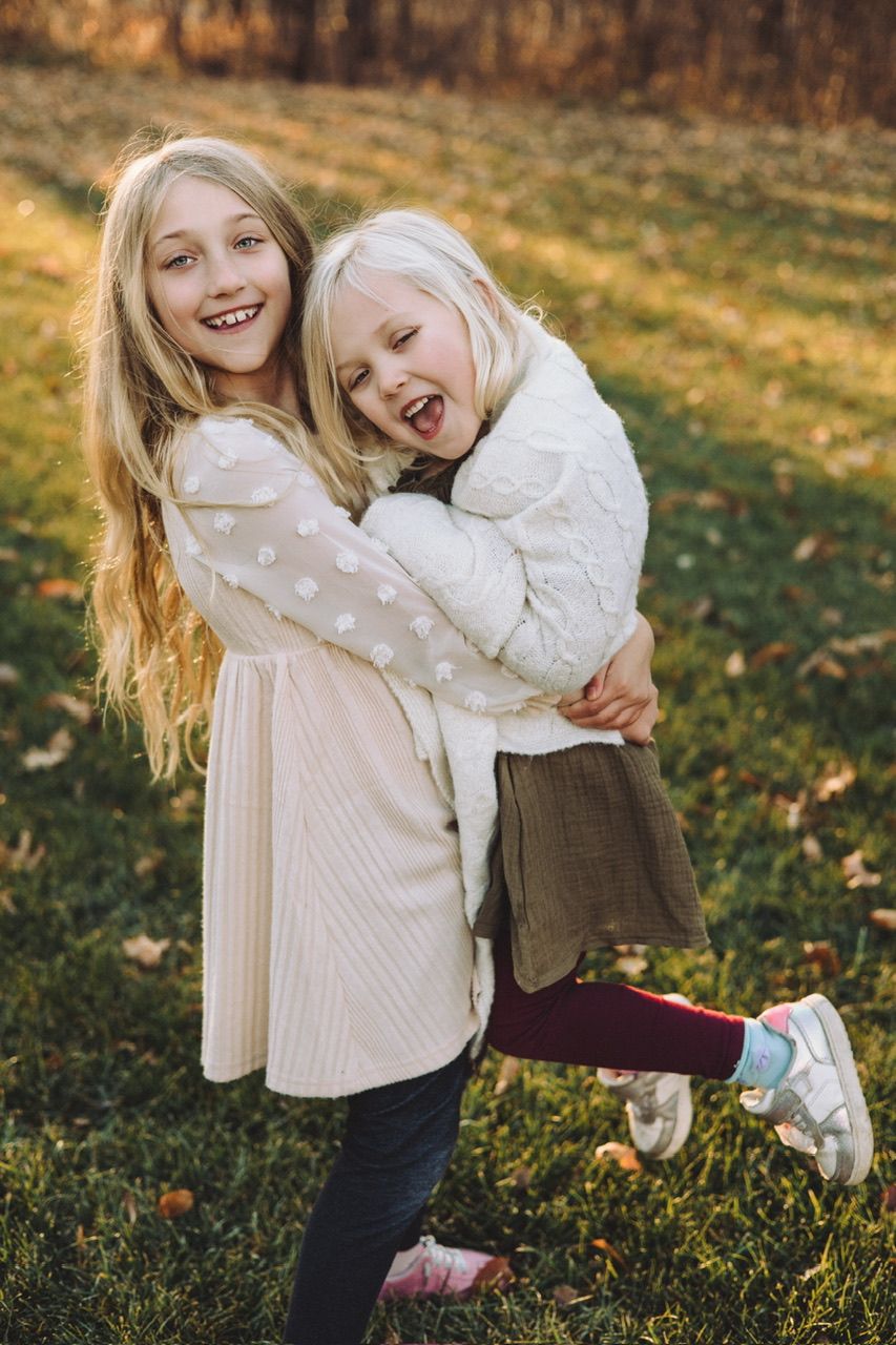 Two people playing and laughing together on autumn grass with fallen leaves.