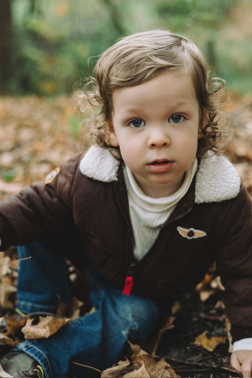 Child in brown coat and white sweater playing in autumn leaves.